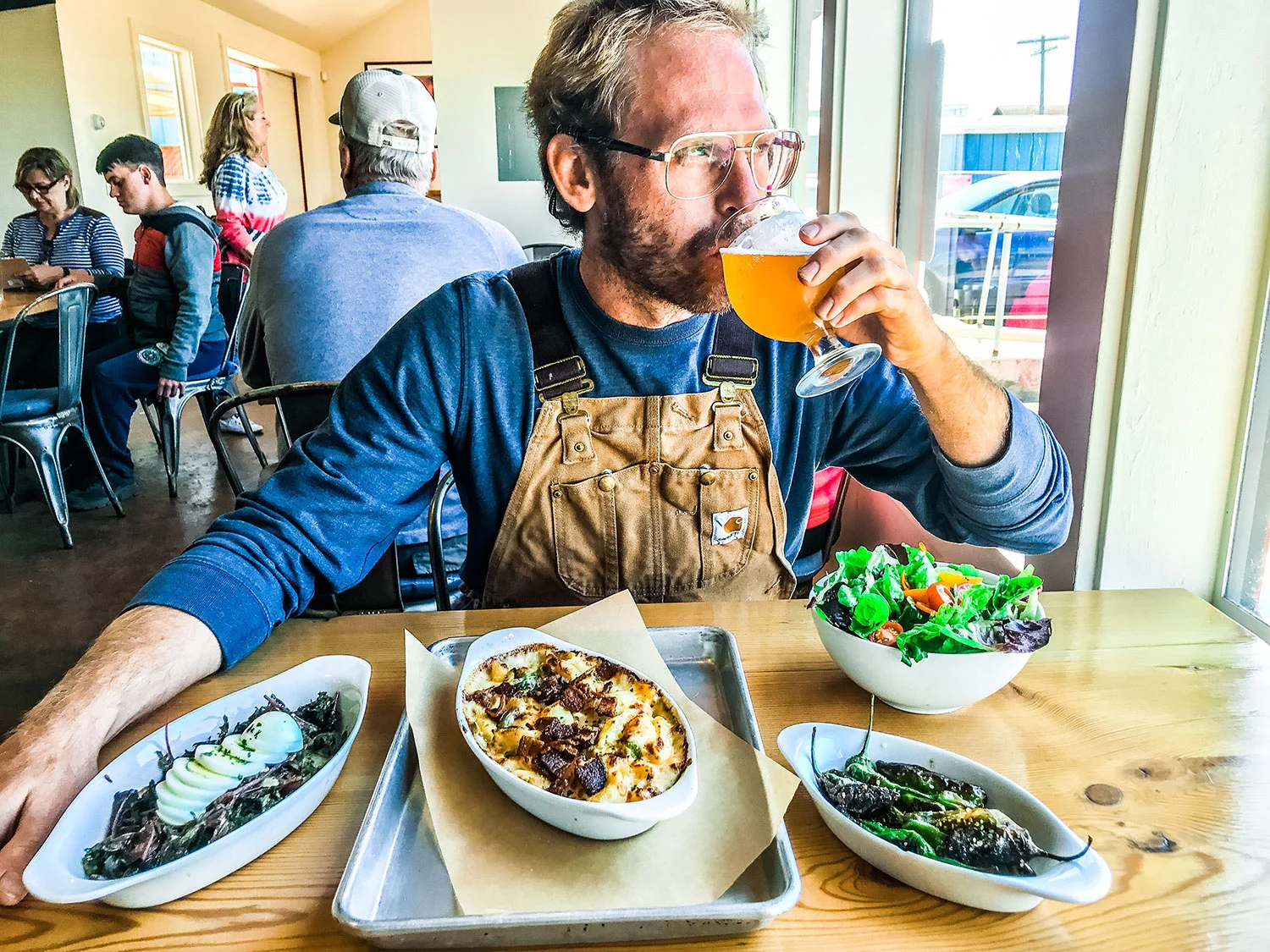 a man sits at Overtime Brewery drinking a beer with an array of dishes in front of him