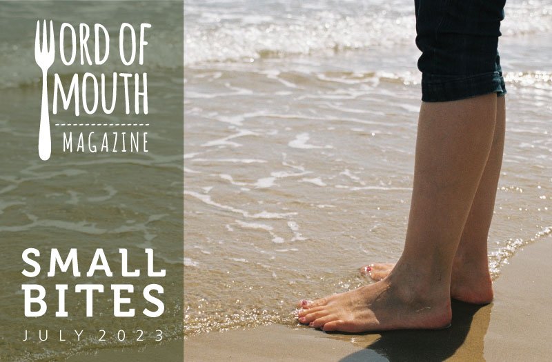 Small Bites July 2023 from Word of Mouth magazine -- image of feet on the sand as a wave slides up to the toes