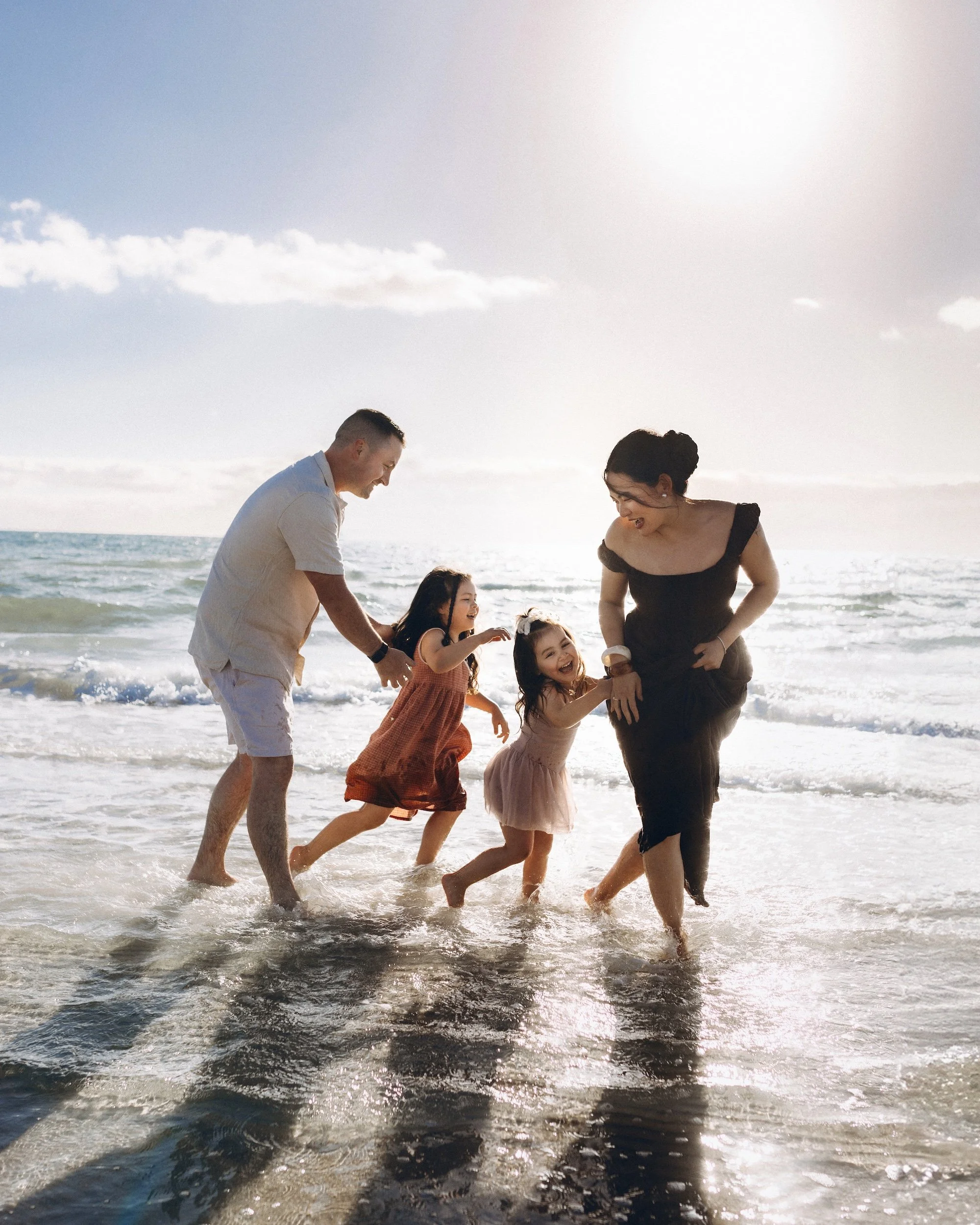 A family with young children play and laugh together during a relaxed outdoor family photography session at a Melbourne beach