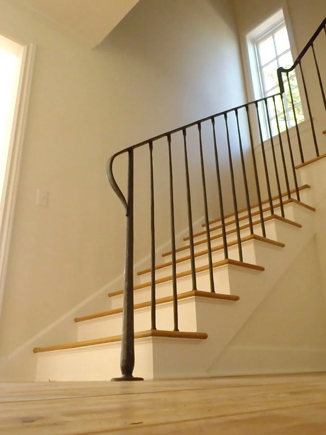 Interior view of a staircase with wooden steps and black metal railing in a house, natural light coming through a window.