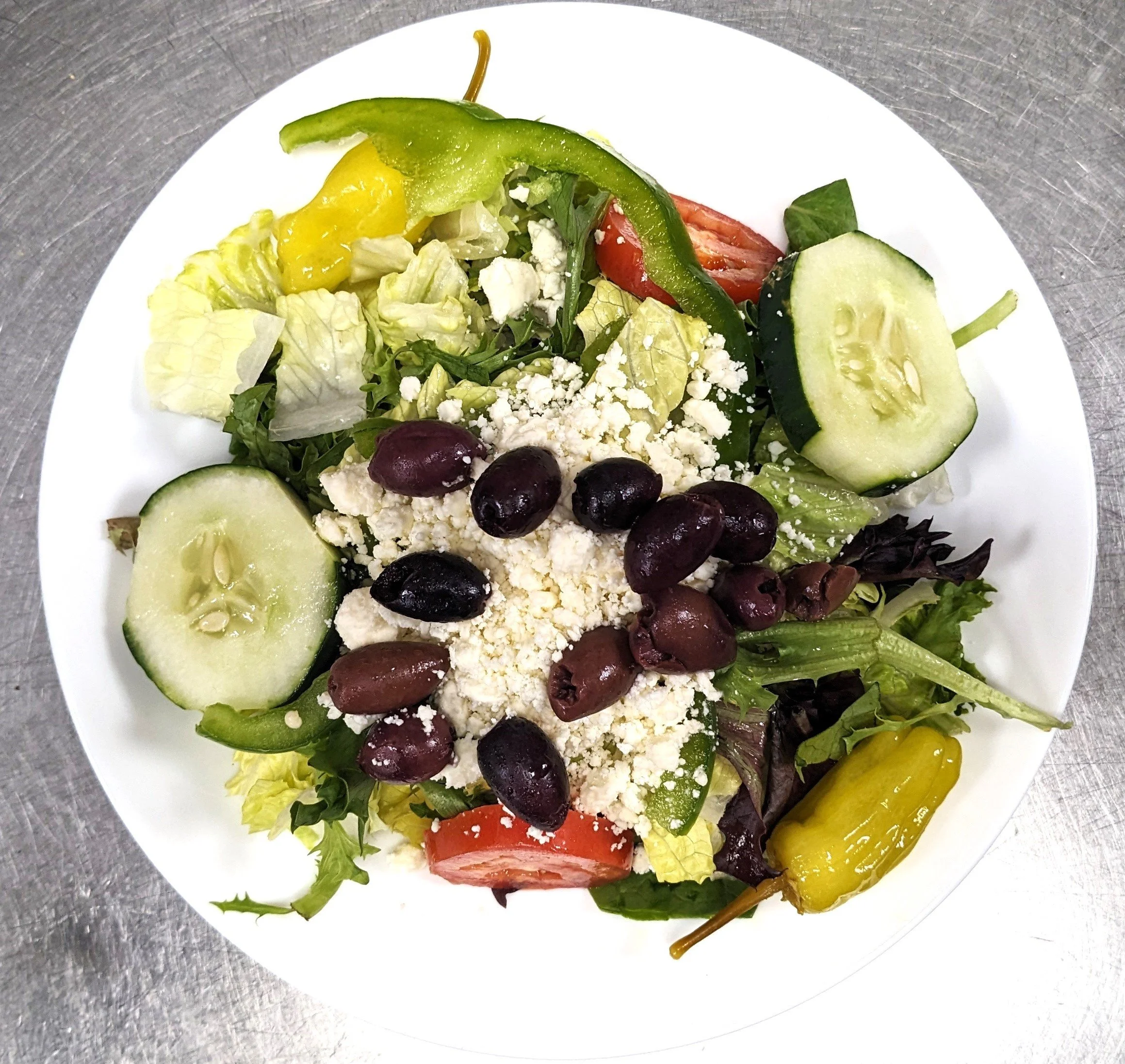 Fresh vegetable salad with cucumbers, tomatoes, bell peppers, black olives, and crumbled cheese on a white plate.