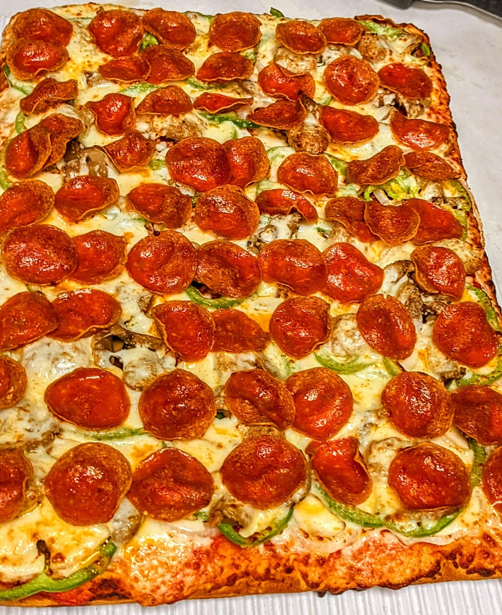 A rectangular pizza topped with slices of pepperoni, green bell peppers, mushrooms, and melted cheese.