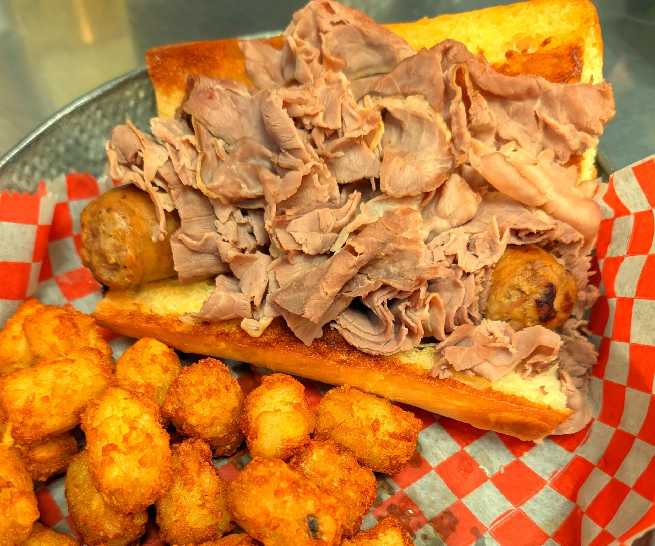 Hot roast beef sandwich with sliced beef, sausage pieces, and bread, served with tater tots.