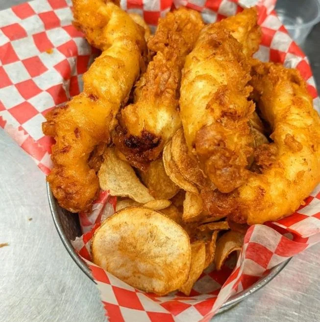 Basket of fried fish, potato chips, and potato slices on red checkered paper.