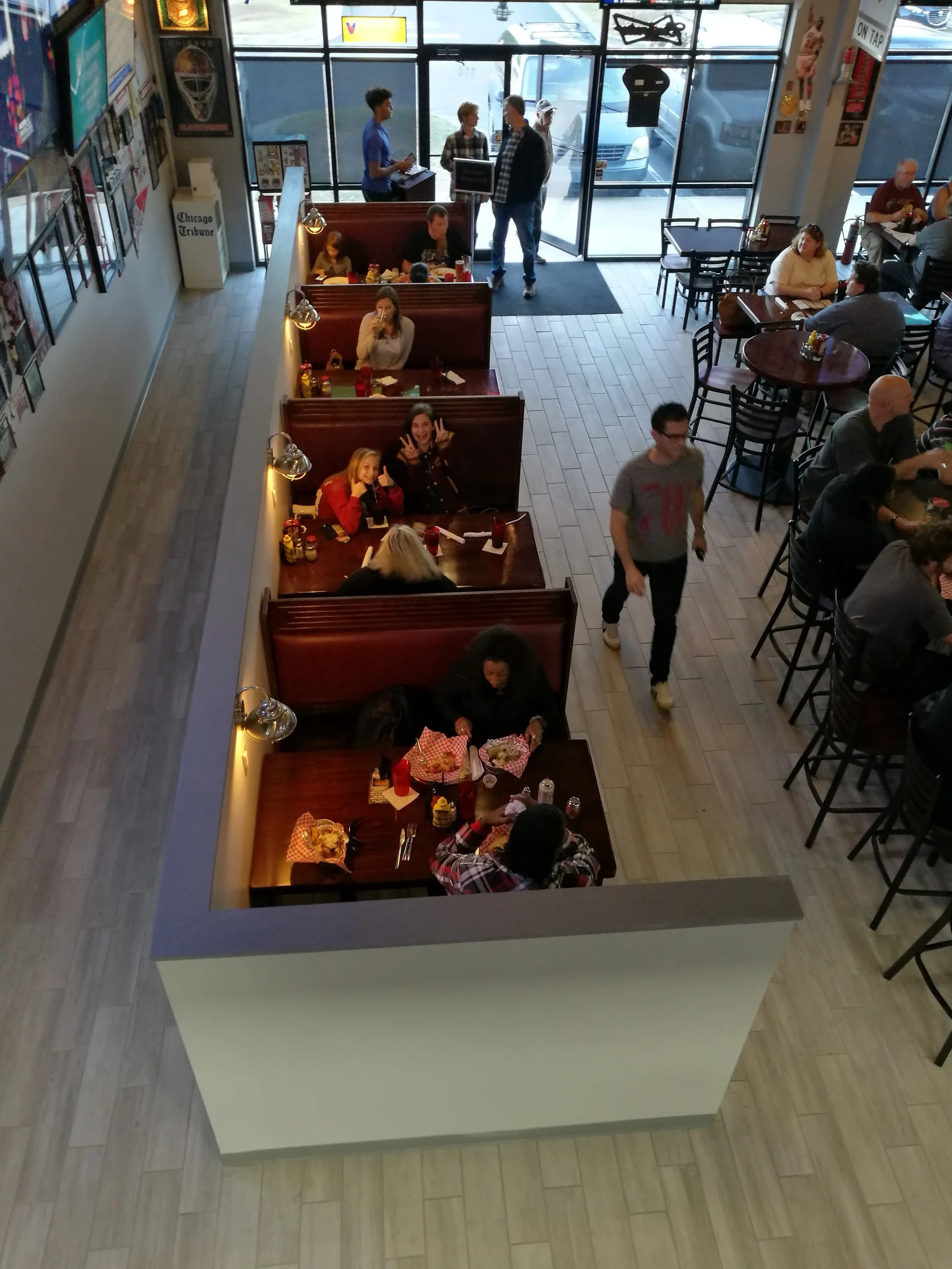 Inside a busy restaurant with booths and tables, some people dining and others ordering at the counter near the large front windows.