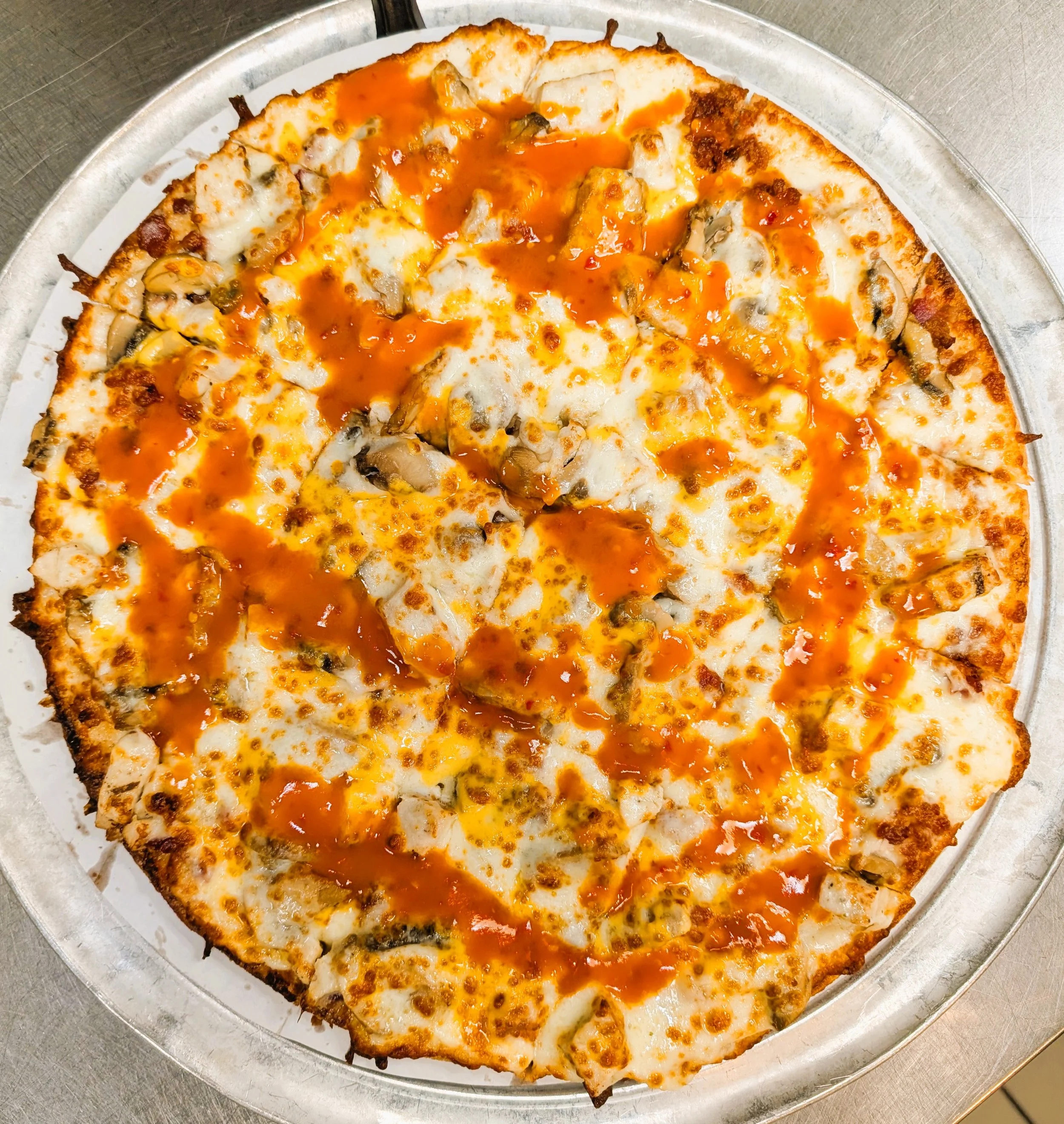 A pizza with cheese, mushrooms, and hot sauce on a silver tray.