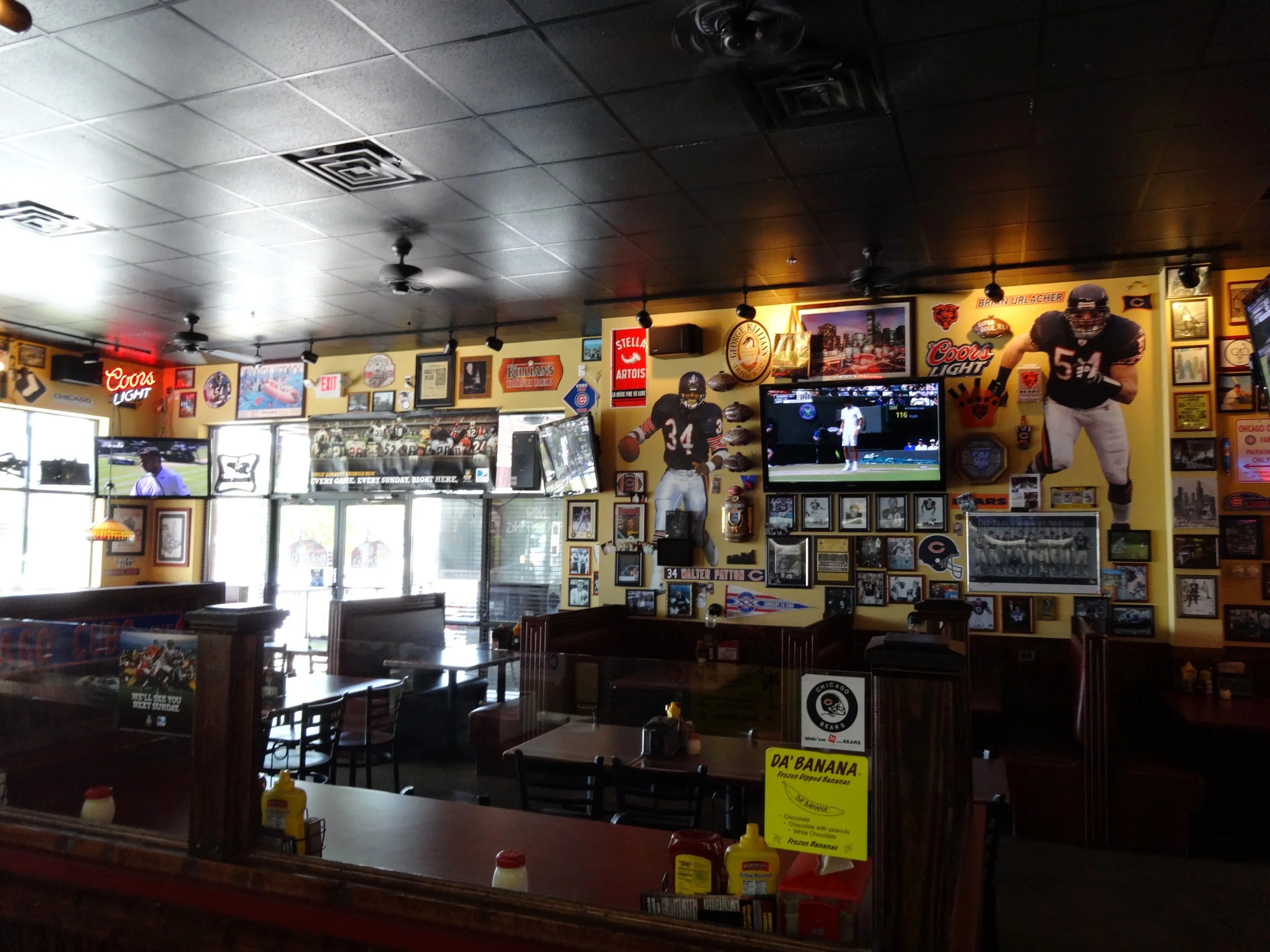 Interior of a sports bar decorated with football memorabilia, including framed photos, jerseys, and large posters of football players, with multiple TVs displaying sports games.