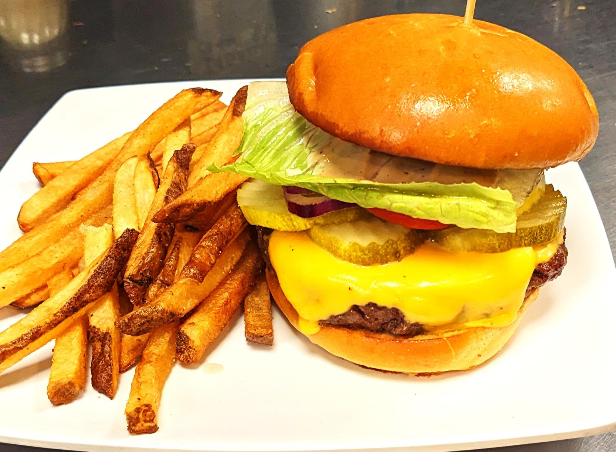 Cheeseburger with lettuce, pickles, tomato, onion, and cheese, served with French fries on a white plate.