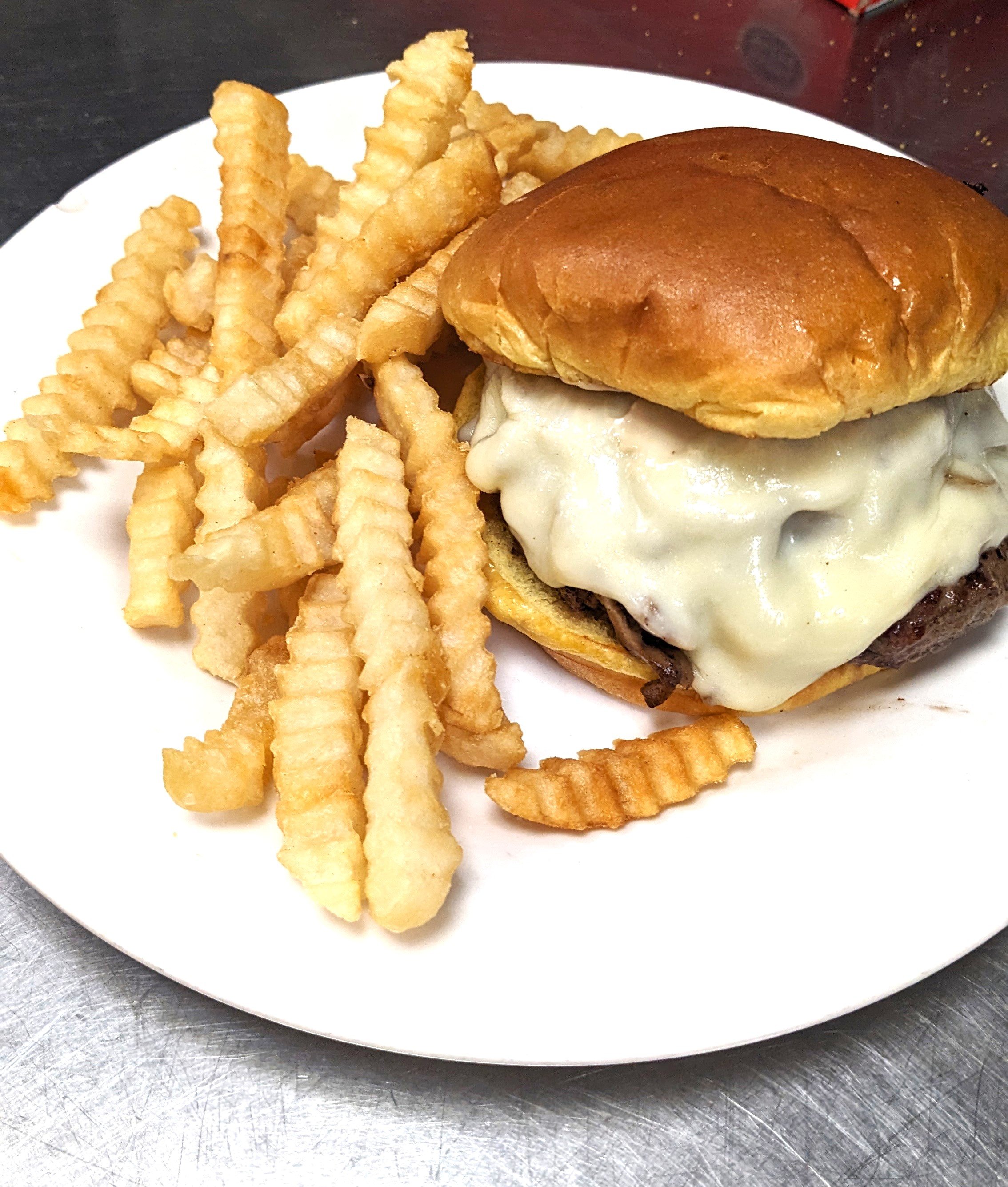A plate with waffle fries and a cheeseburger with melted cheese, beef patty, and bun