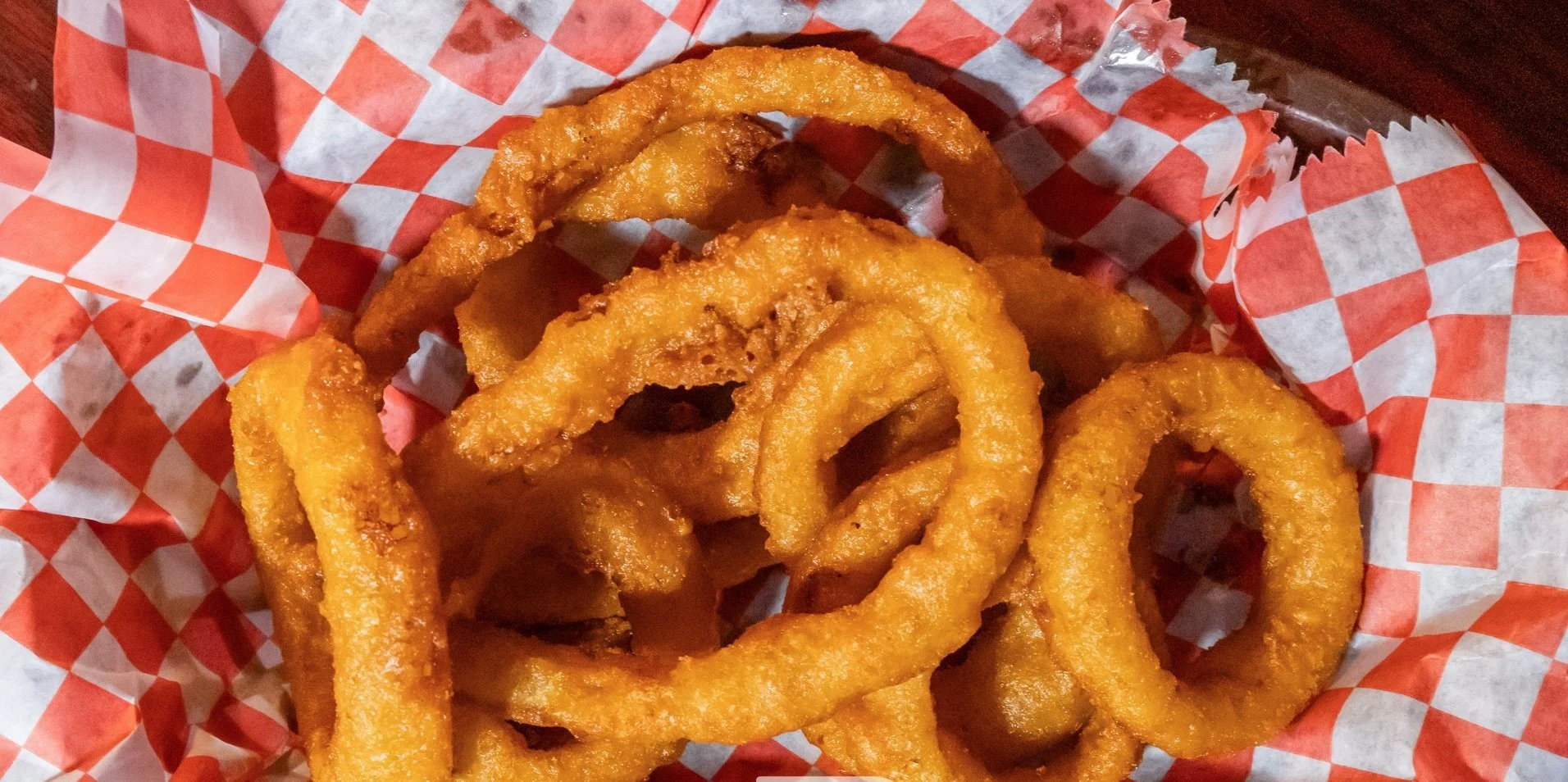 Golden fried onion rings in a basket lined with red and white checkered paper.