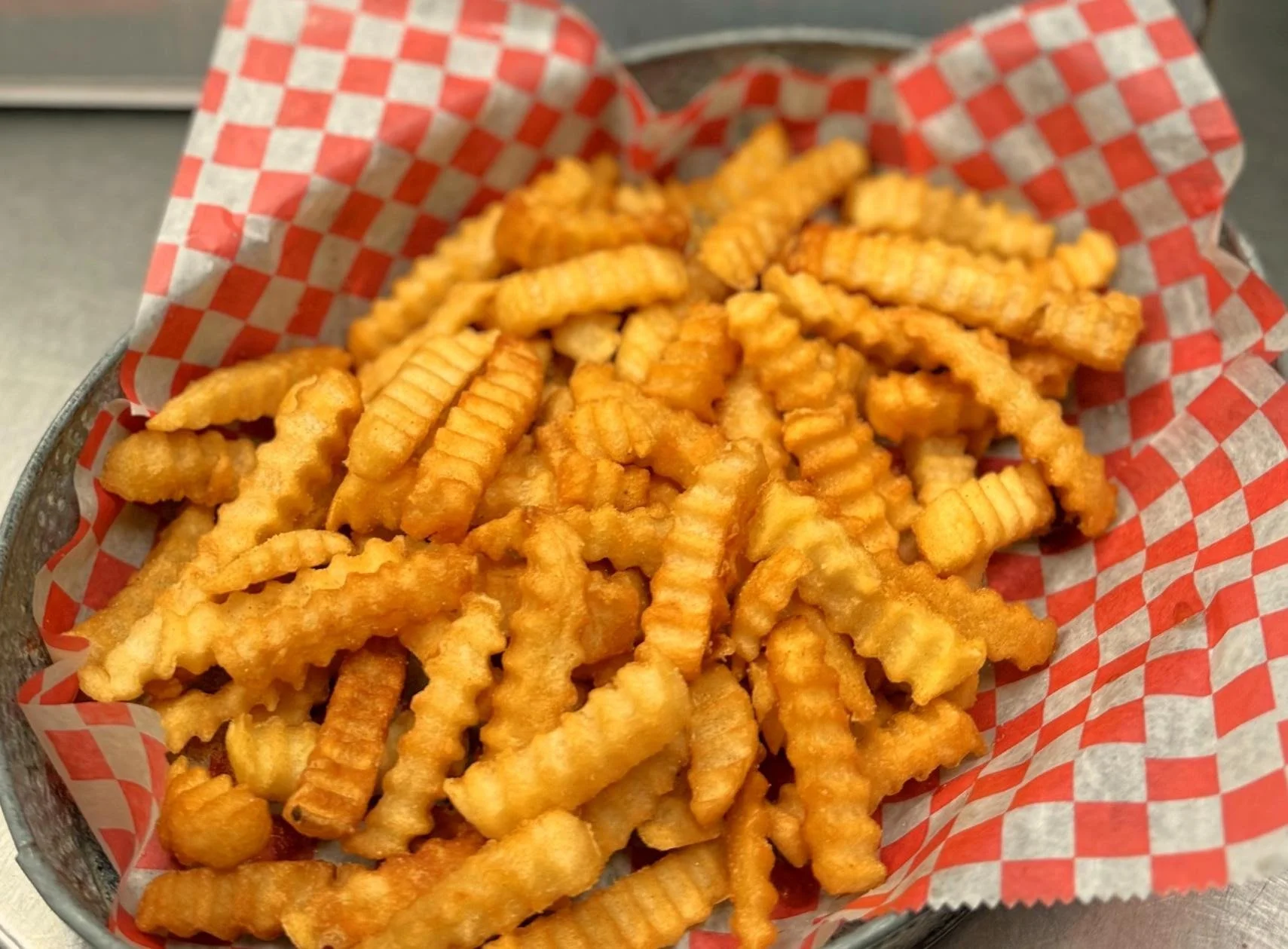 Basket of crinkle-cut French fries lined with red and white checkered paper