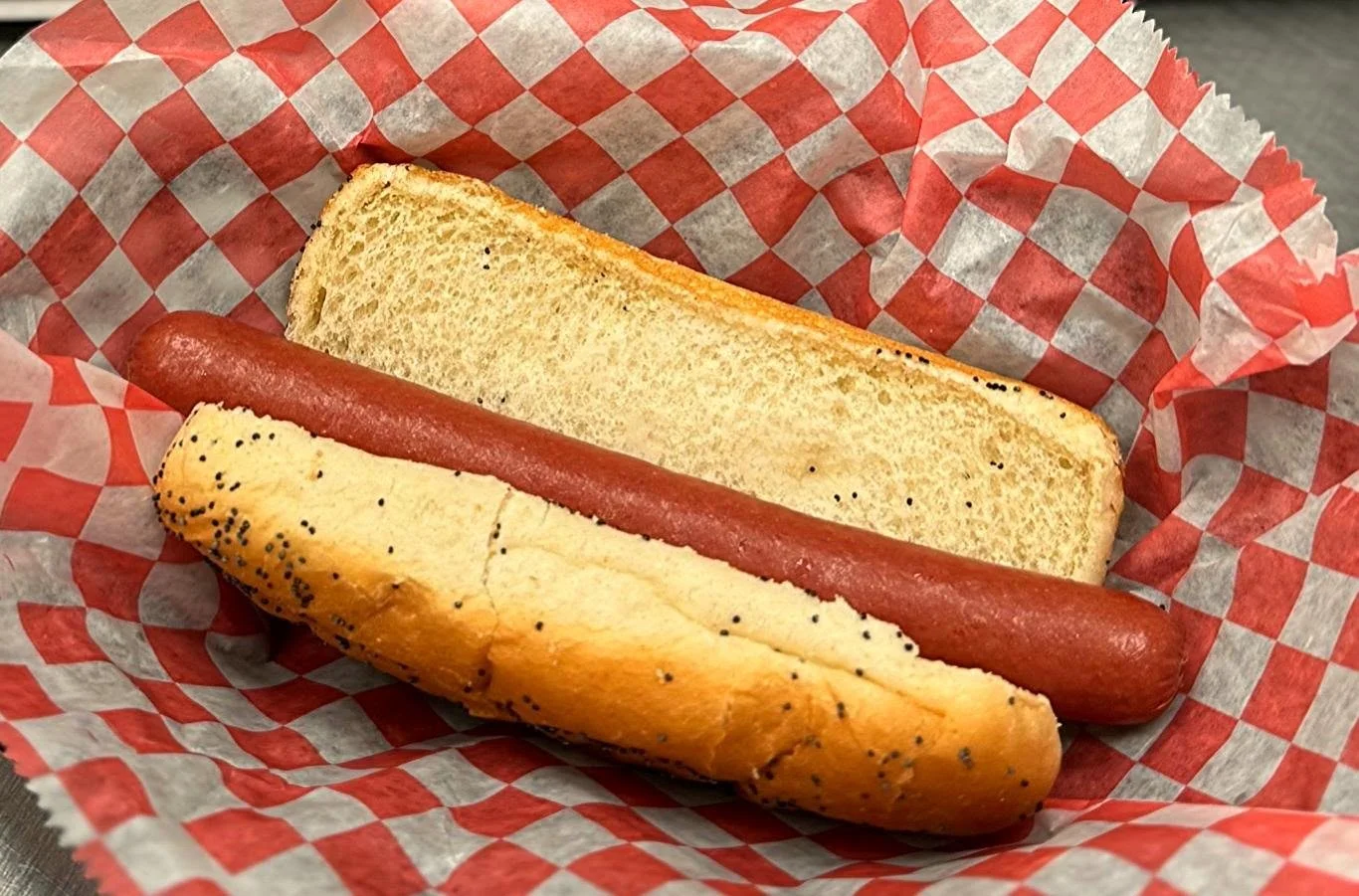 Hot dog in a poppy seed bun and a hot dog bun without a hot dog, in red and white checkered paper