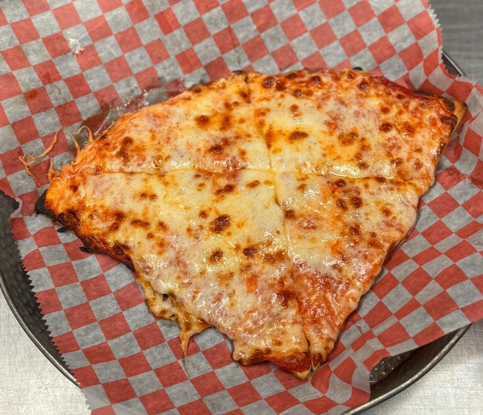 A slice of cheese pizza on checkered paper in a black tray.