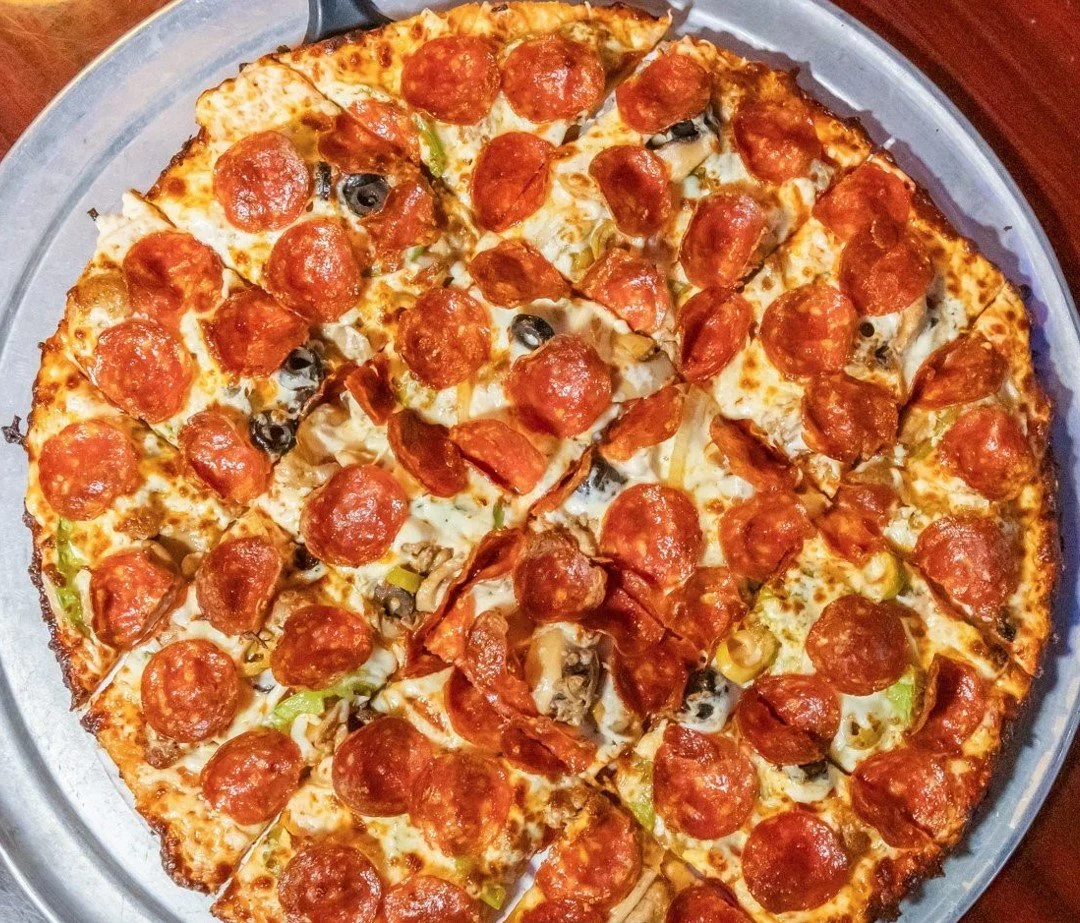 A whole pepperoni pizza with cheese, mushrooms, black olives, and green peppers on a silver tray.