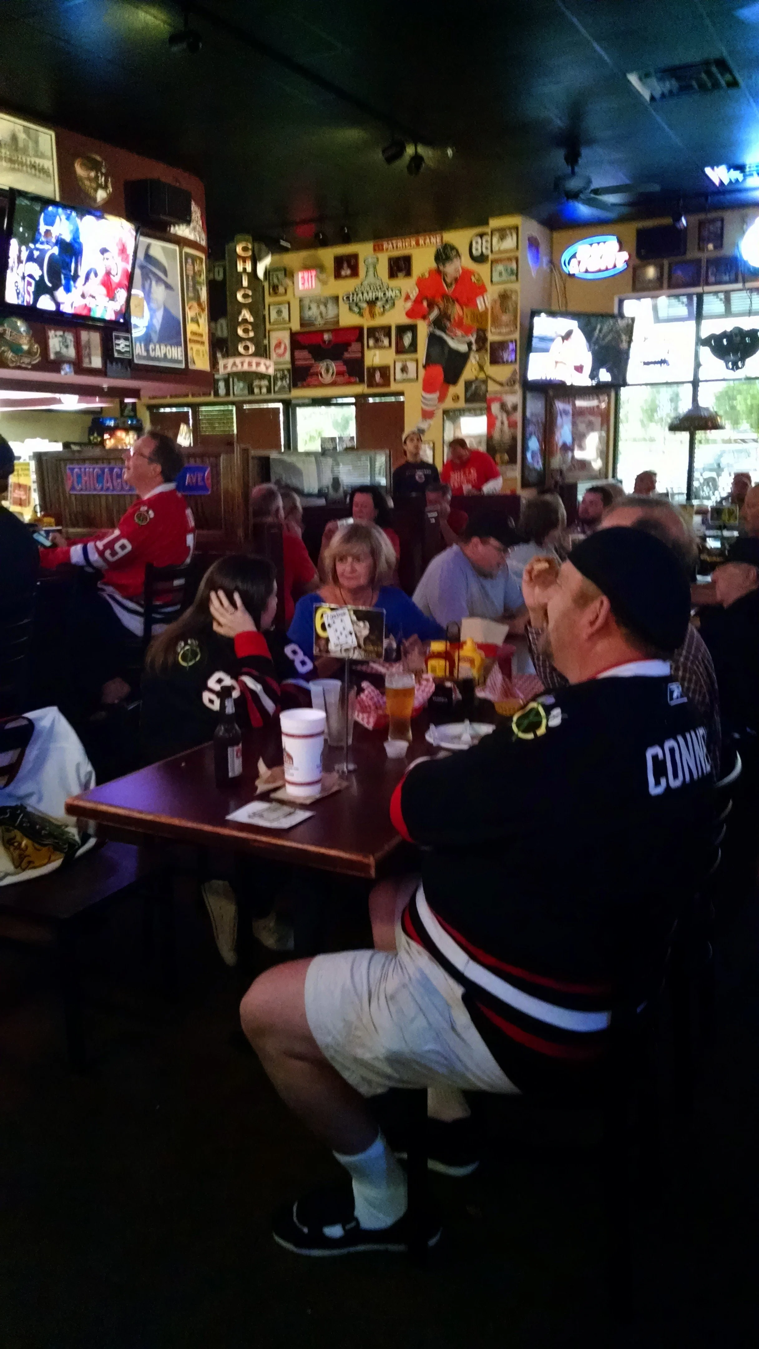 People watching a hockey game at a sports bar, wearing Chicago Blackhawks jerseys, with hockey memorabilia and images of hockey players on the walls.