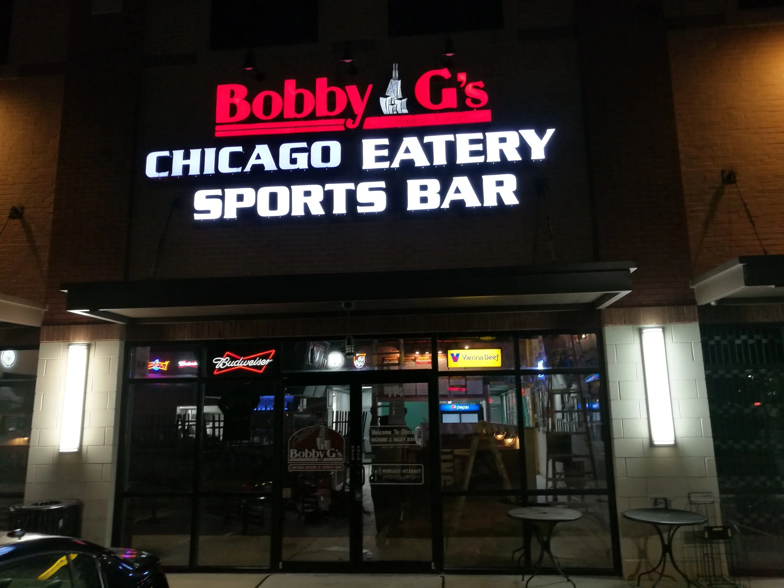 Night view of Bobby G's Chicago Eatery Sports Bar exterior with illuminated sign and glass doors