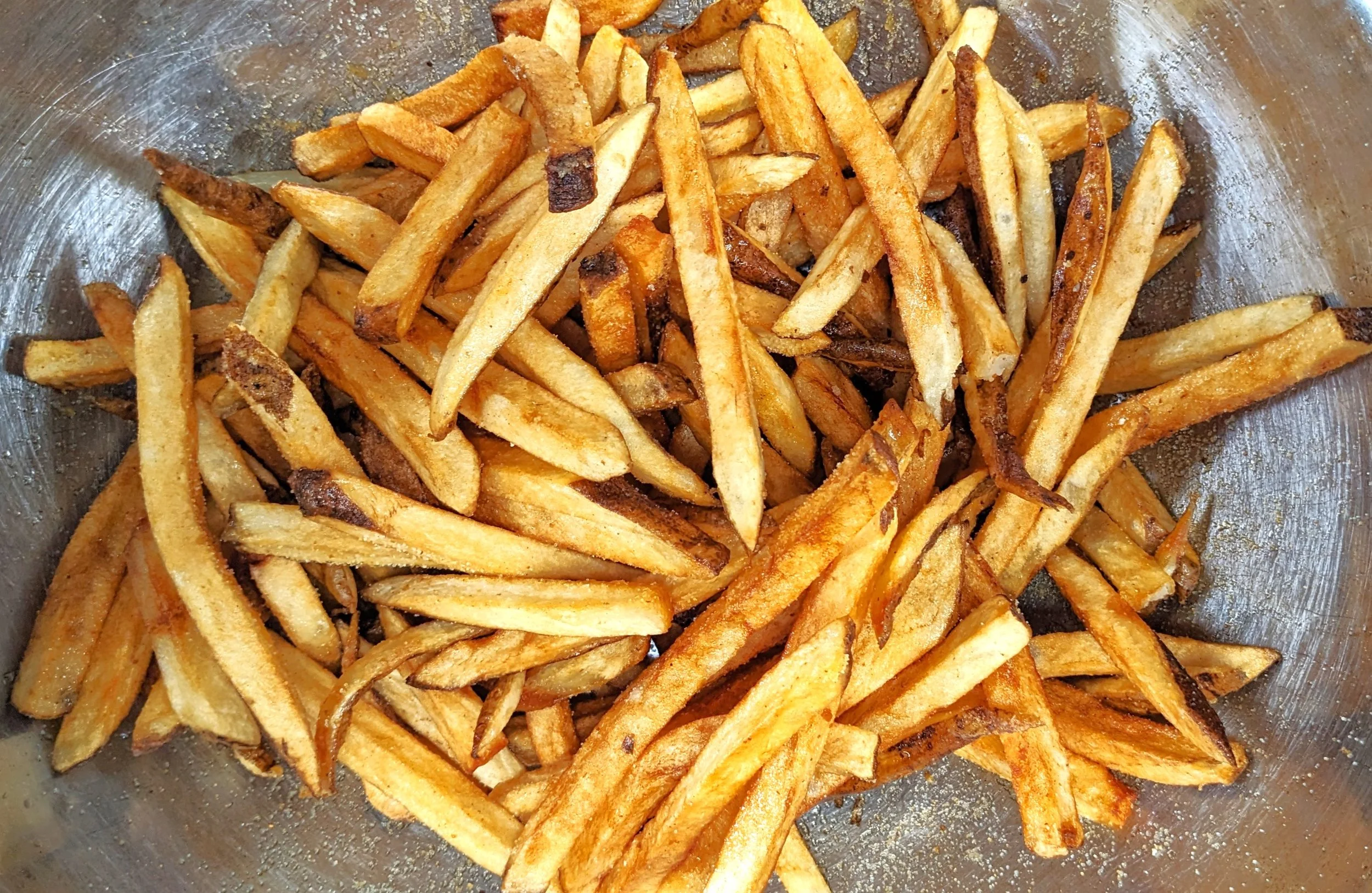 Cooked French fries in a metal bowl with some slight charring on some fries.