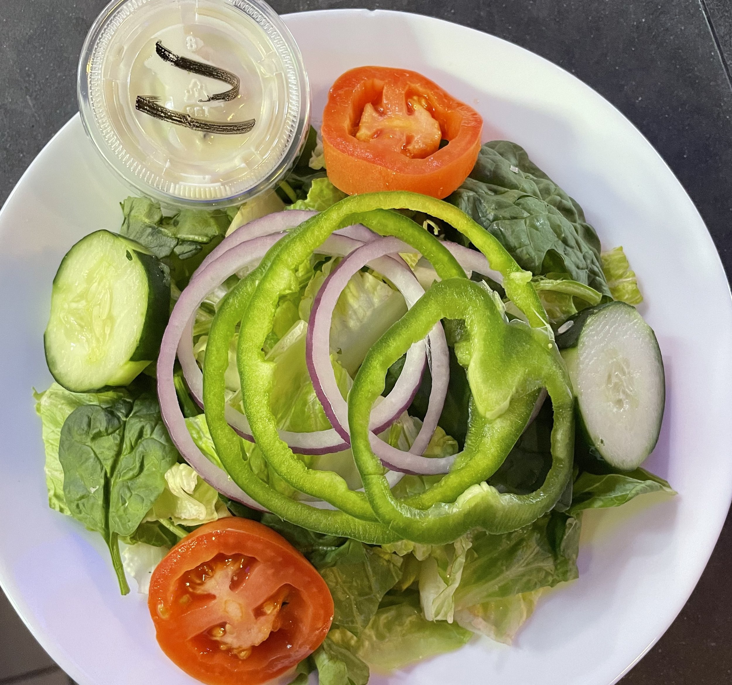 Fresh garden salad with lettuce, cucumber, tomato, and onion slices, served with a small container of salad dressing.