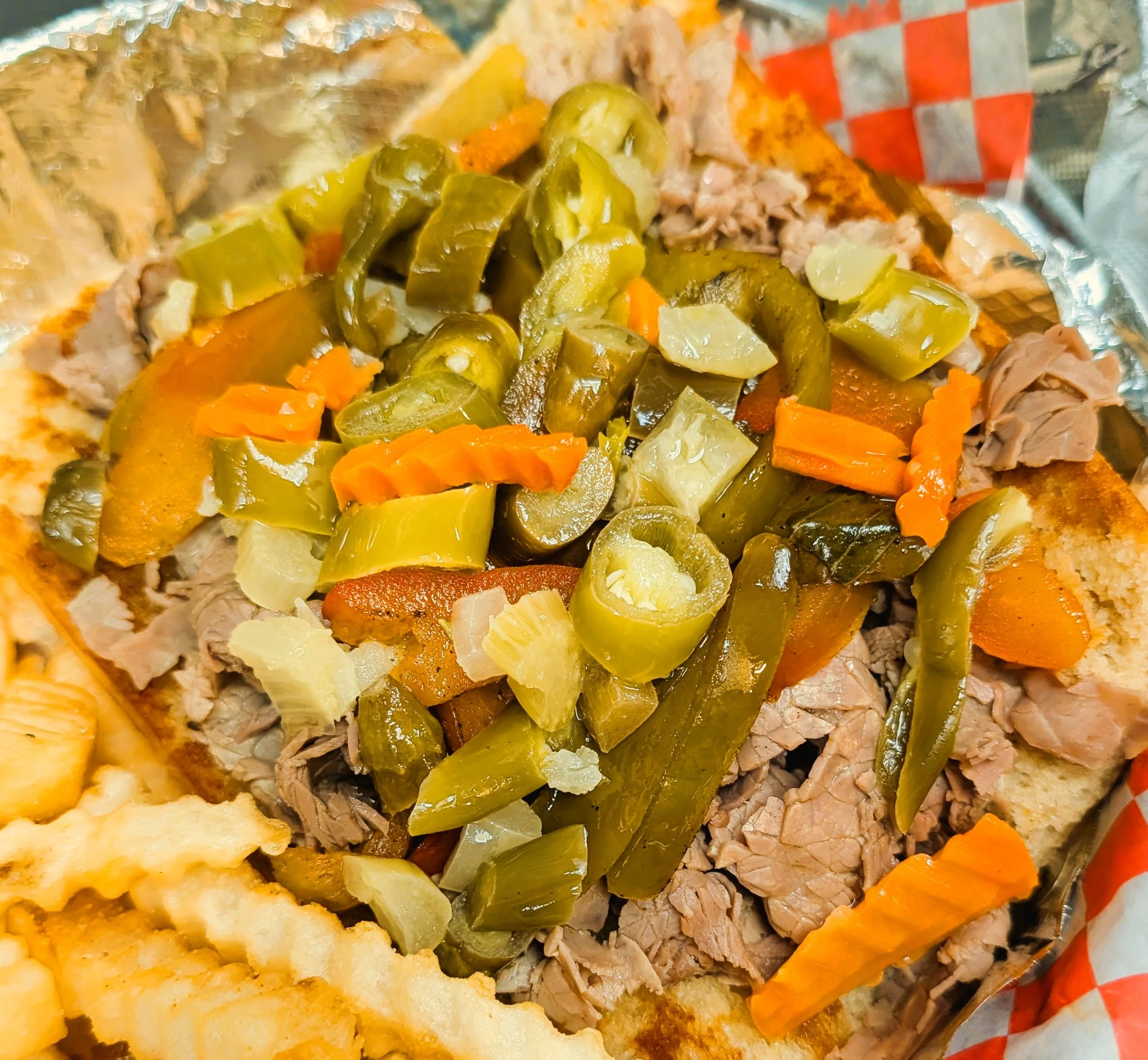Open-faced sandwich with chopped pickles, shredded meat, and vegetables on bread inside foil.