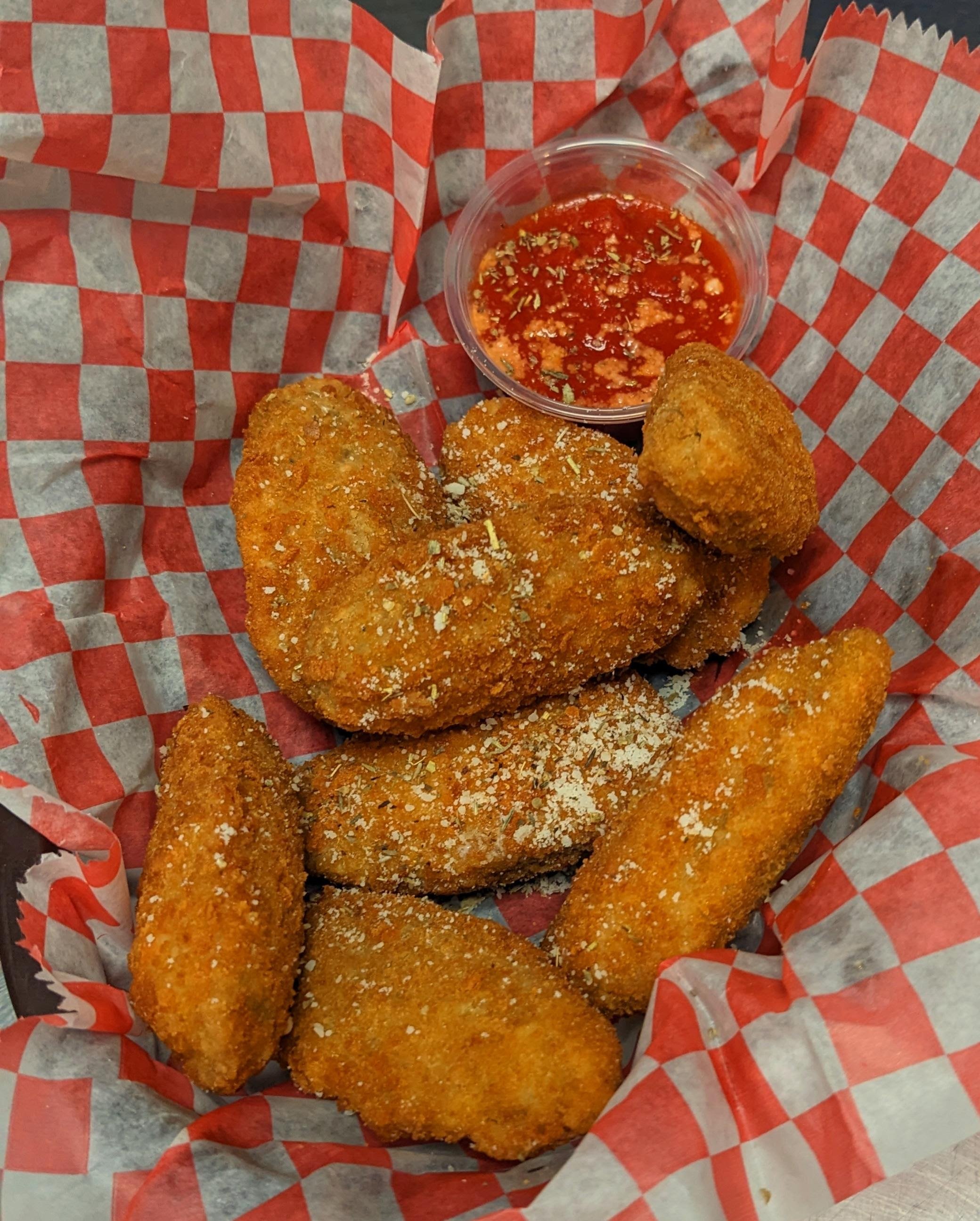 A basket of fried chicken tenders and chicken nugget with a cup of dipping sauce.