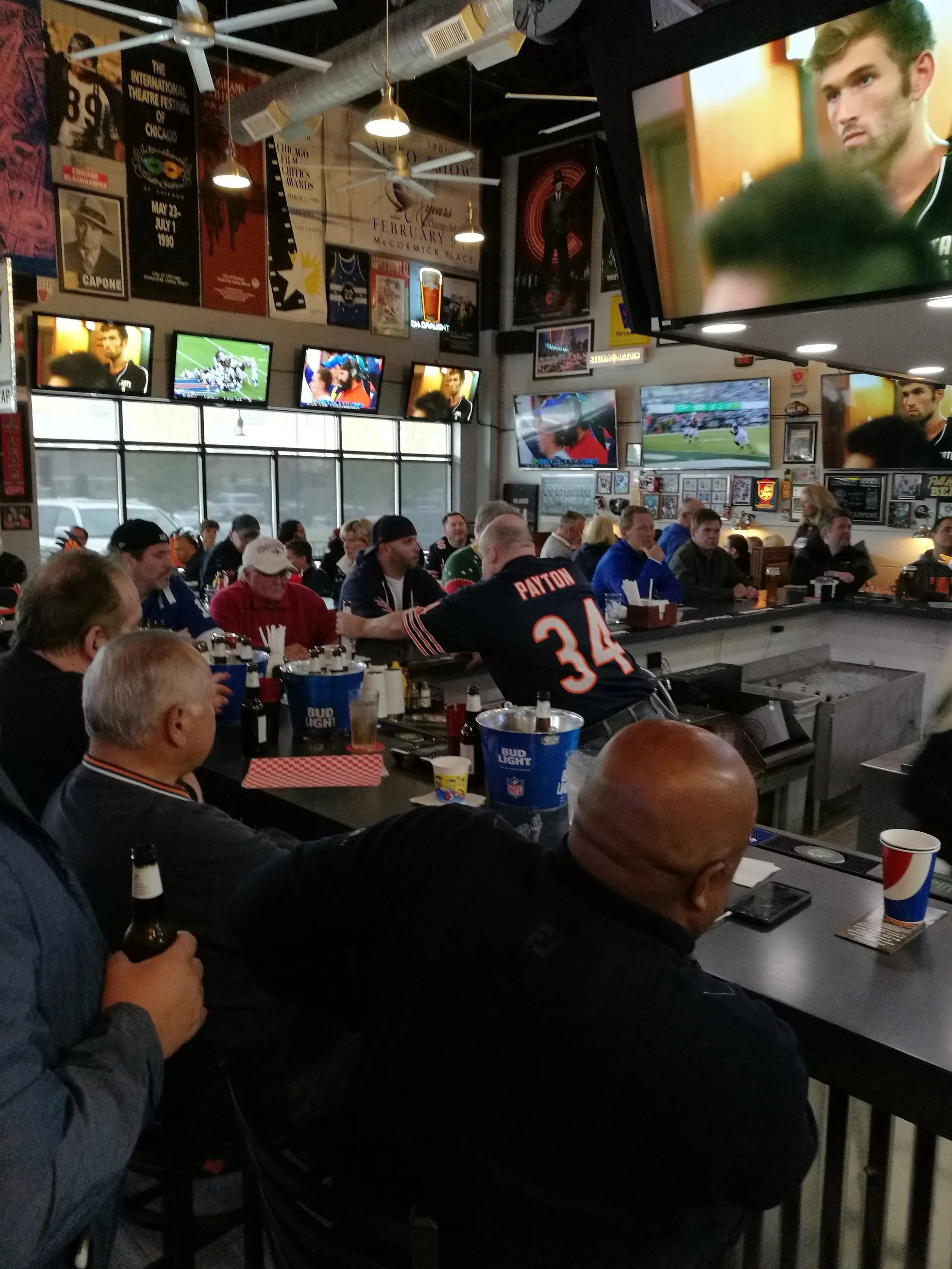People watching sports games on multiple TVs in a sports bar, with posters and banners on the walls and beers on the tables.