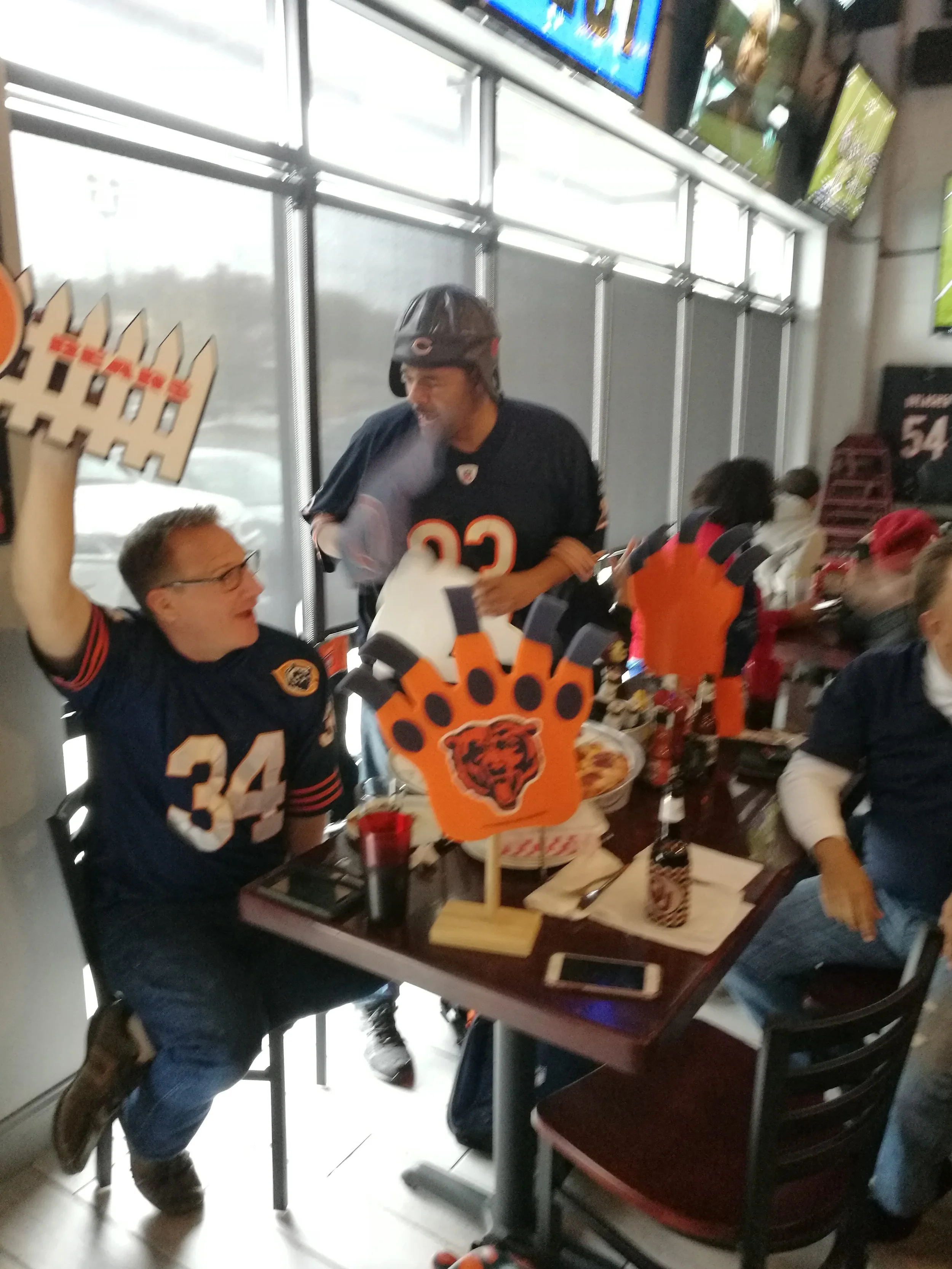 People celebrating a sports game at a restaurant with Detroit Lions themed decorations, including orange paw print centerpieces and jerseys.