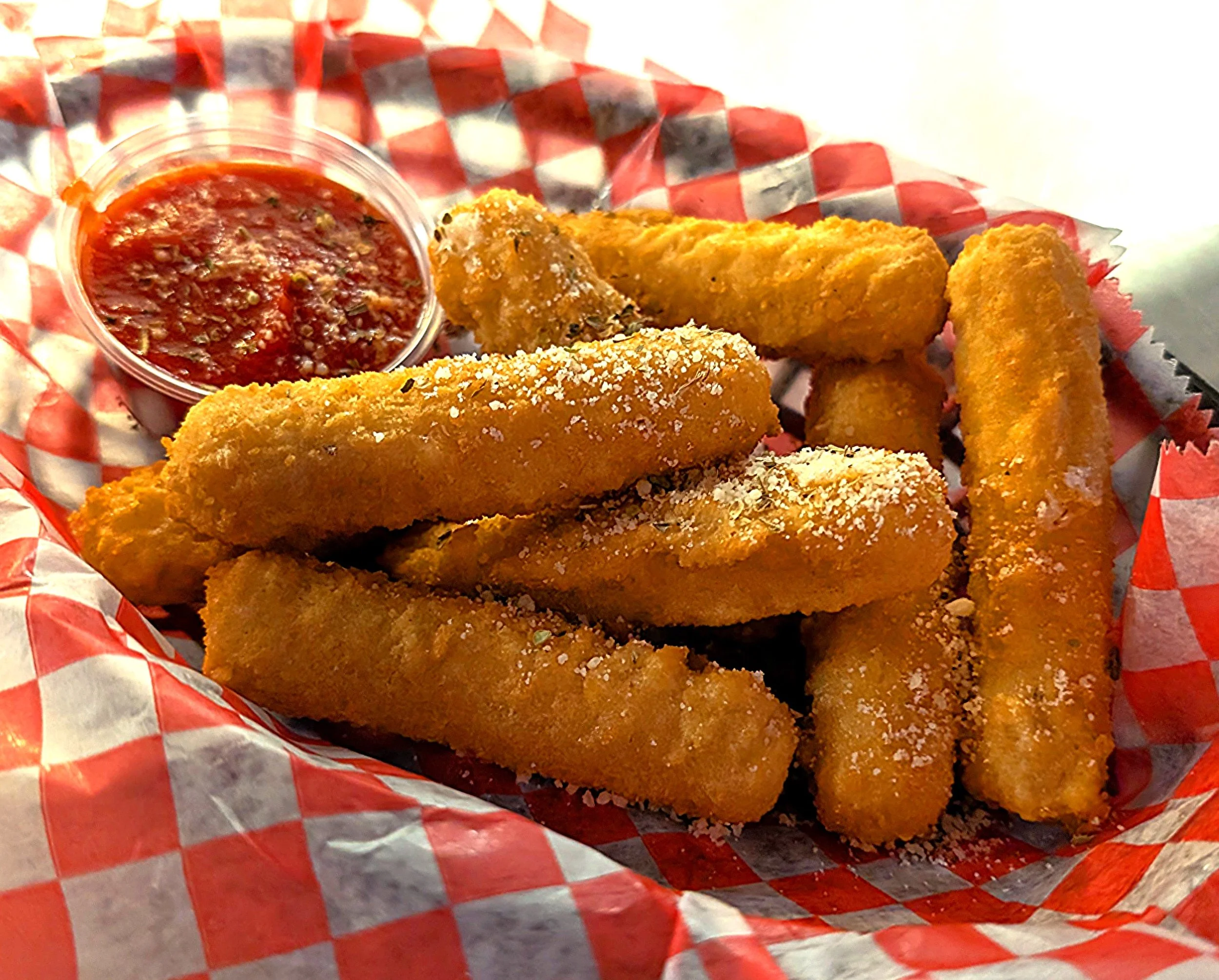 A basket of golden fried mozzarella sticks with grated cheese on top, served with a side of marinara sauce.