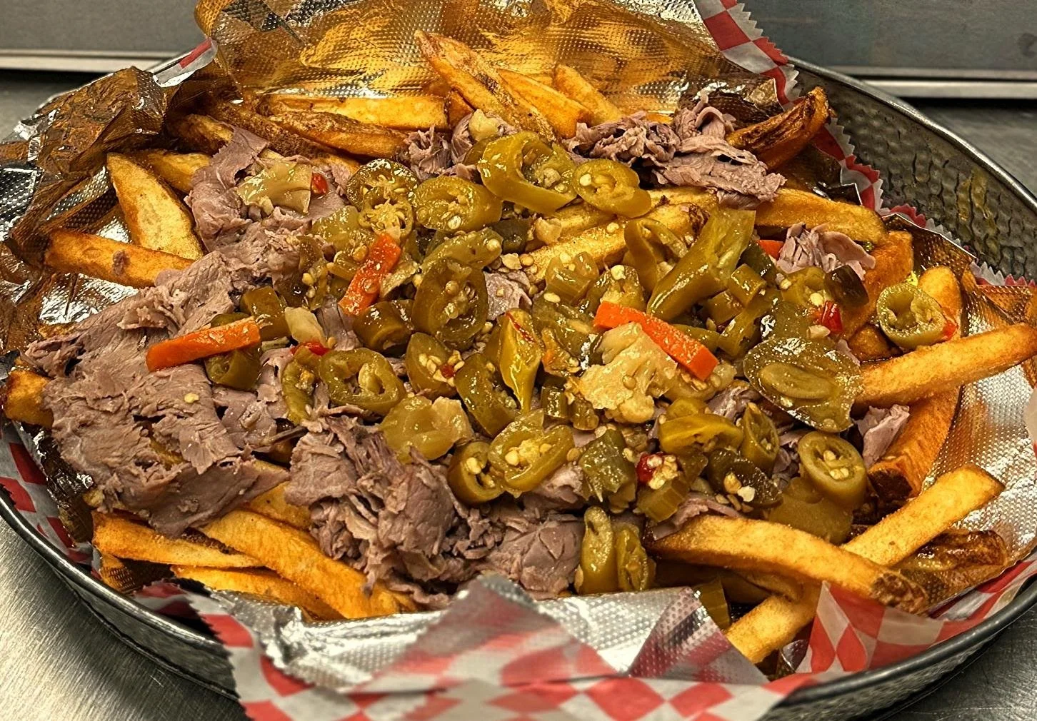 Basket of French fries topped with shredded beef, sliced jalapeños, and chopped pickled peppers on a paper-lined tray.