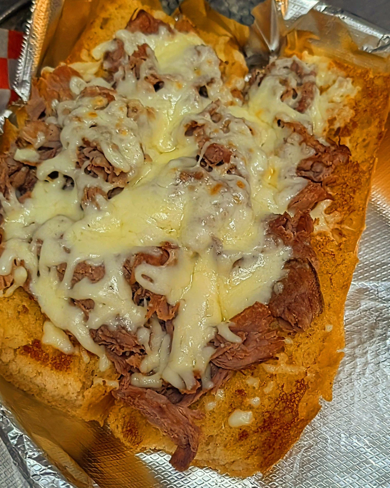 Cheesy beef enchilada casserole with shredded cheese on top and a crispy tortilla base, served on a foil-lined tray.