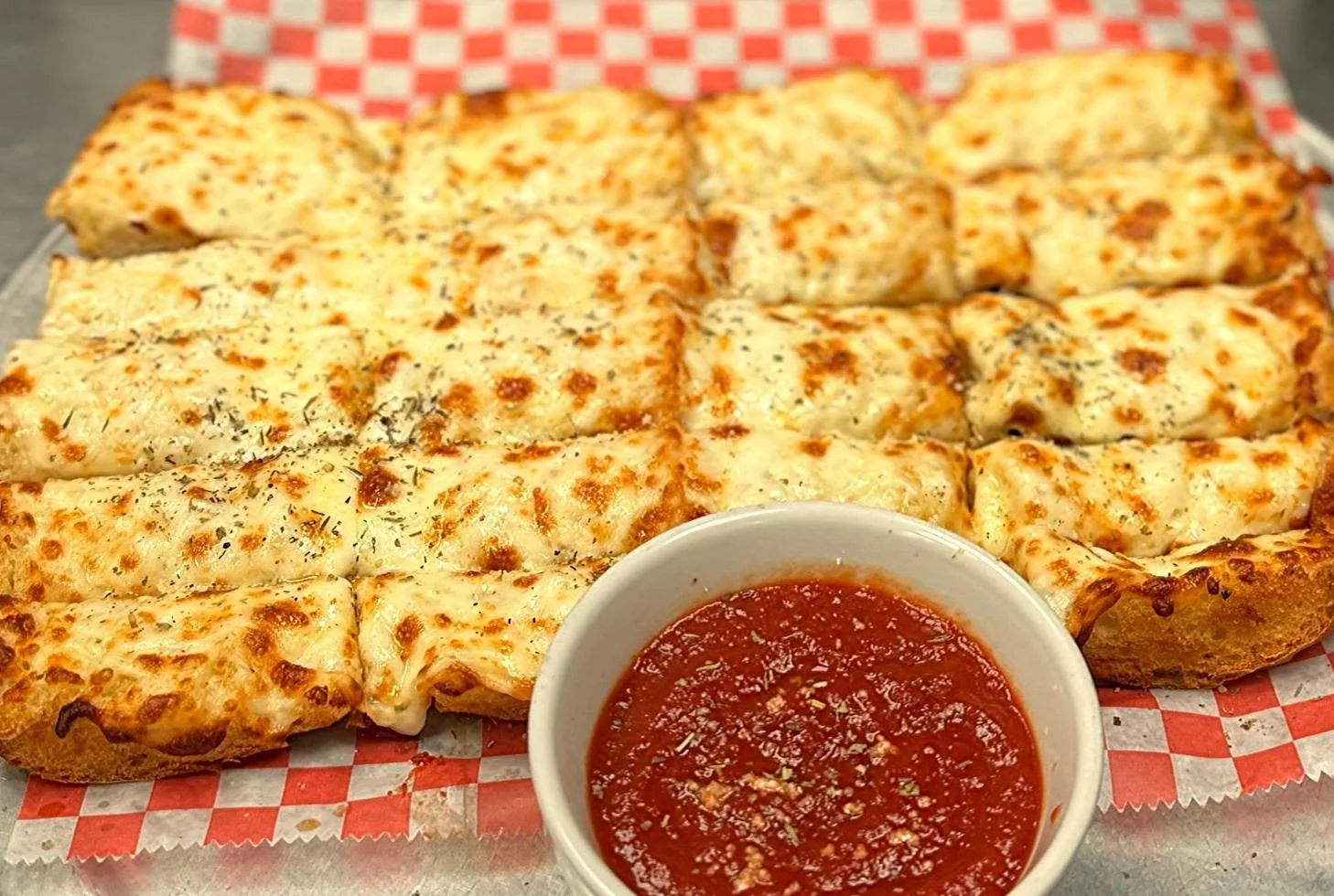 Baked cheesy garlic bread slices with a side of marinara sauce in a white bowl