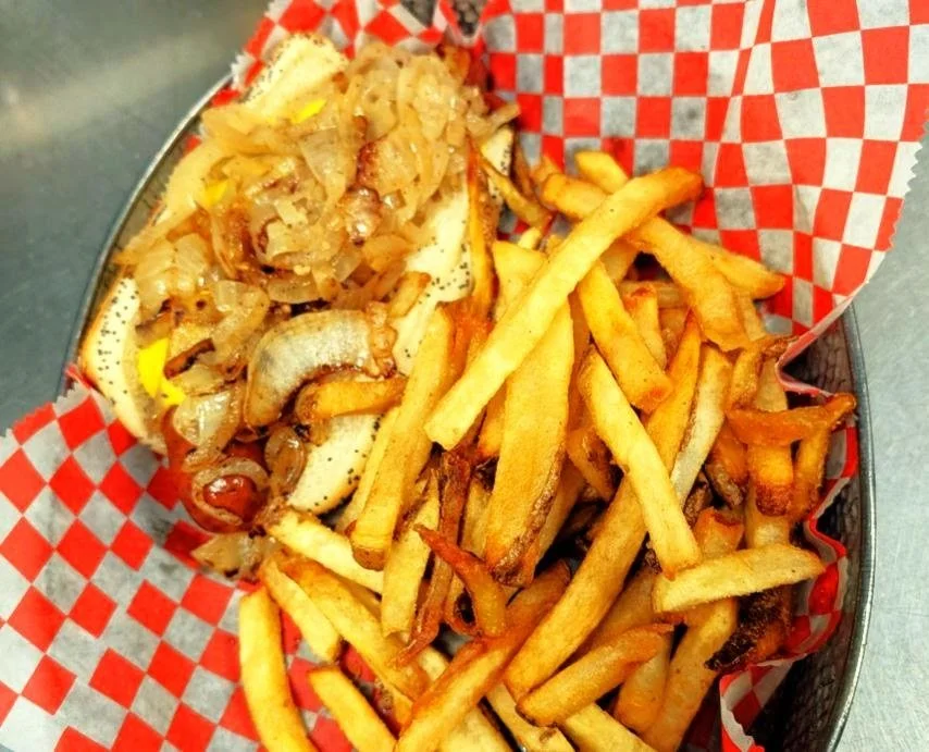 Fried French fries topped with sauteed onions, served in a checkered red and white paper-lined basket.