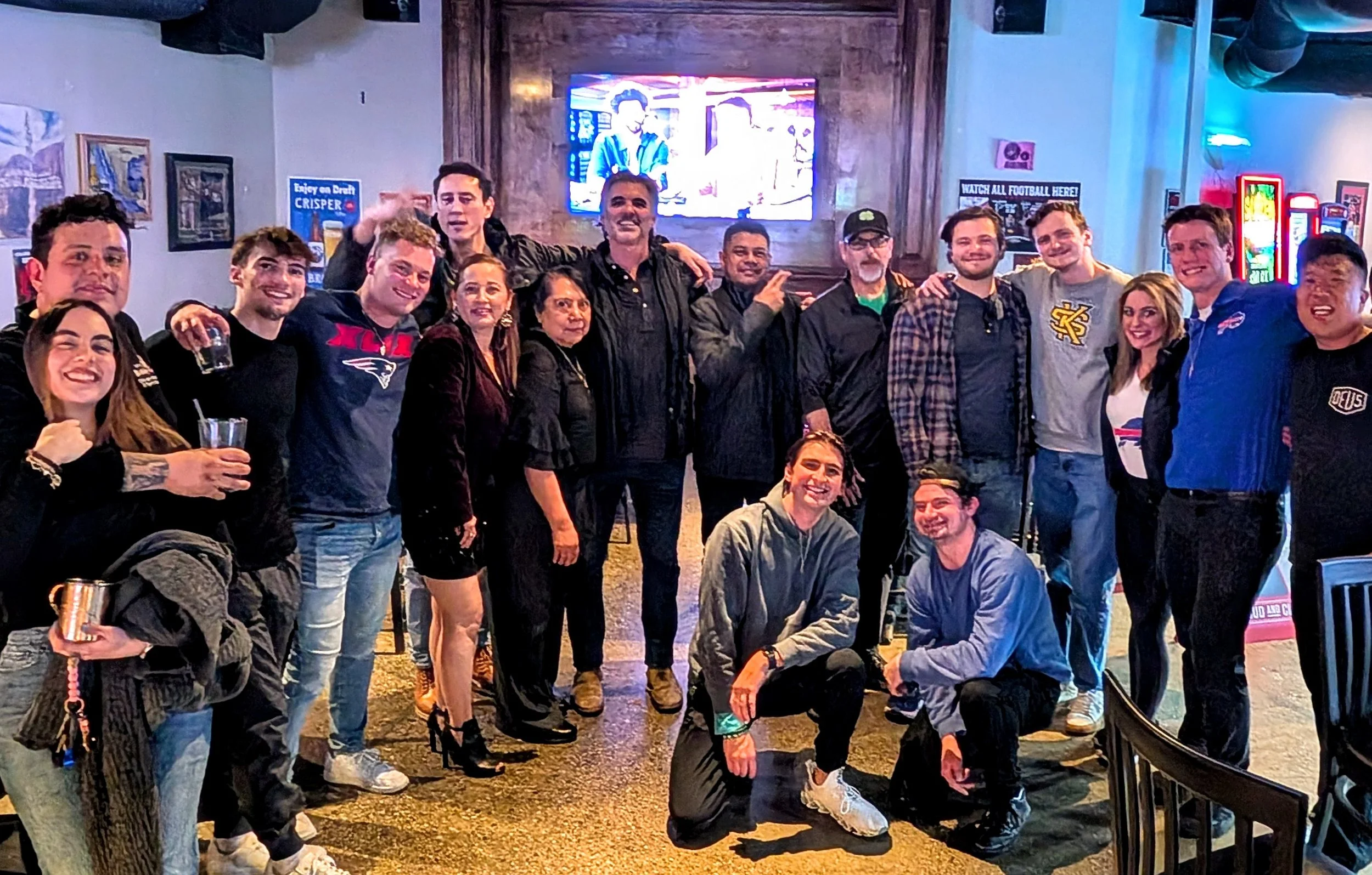A group of people in a bar, smiling and posing for a photo, with some holding drinks.