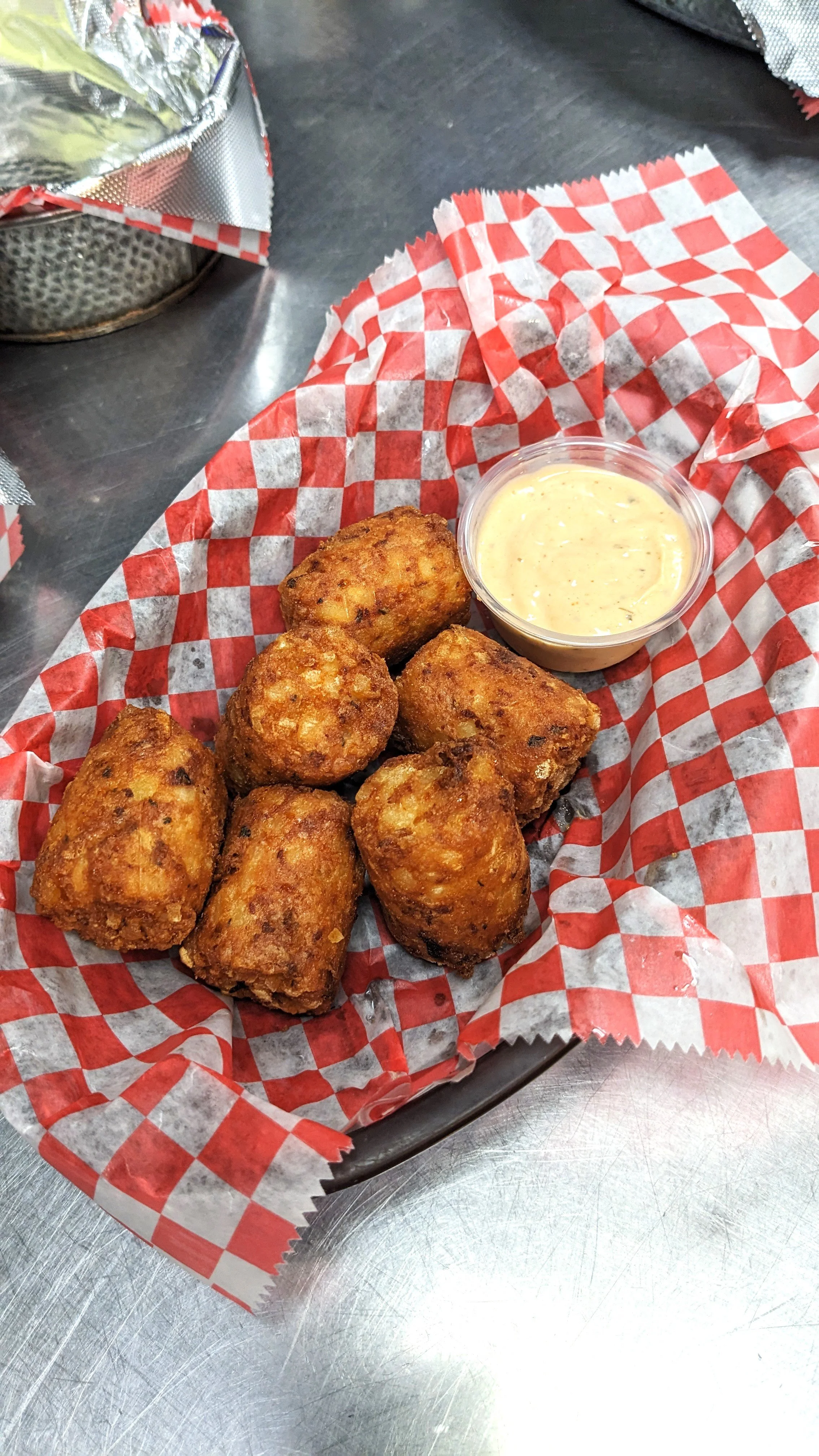 Six fried cheese curds with a side of dipping sauce on red checkered paper in a basket.