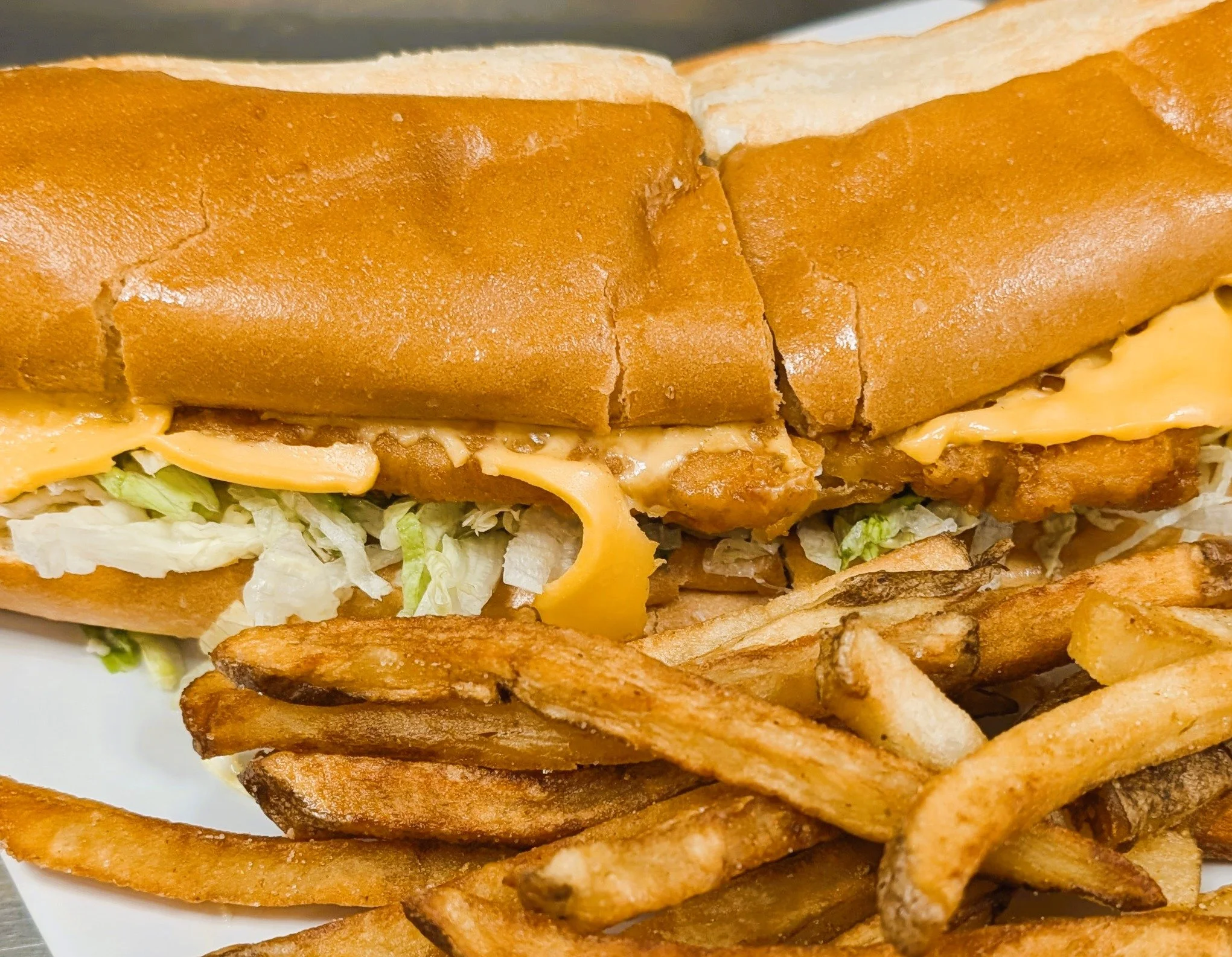 Close-up of a fried chicken sandwich with lettuce, cheddar cheese, and a brioche bun, served with French fries.