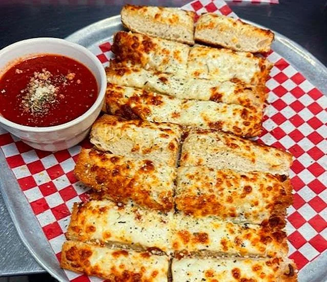 Cheese sticks with marinara dipping sauce on a tray with red checkered paper.