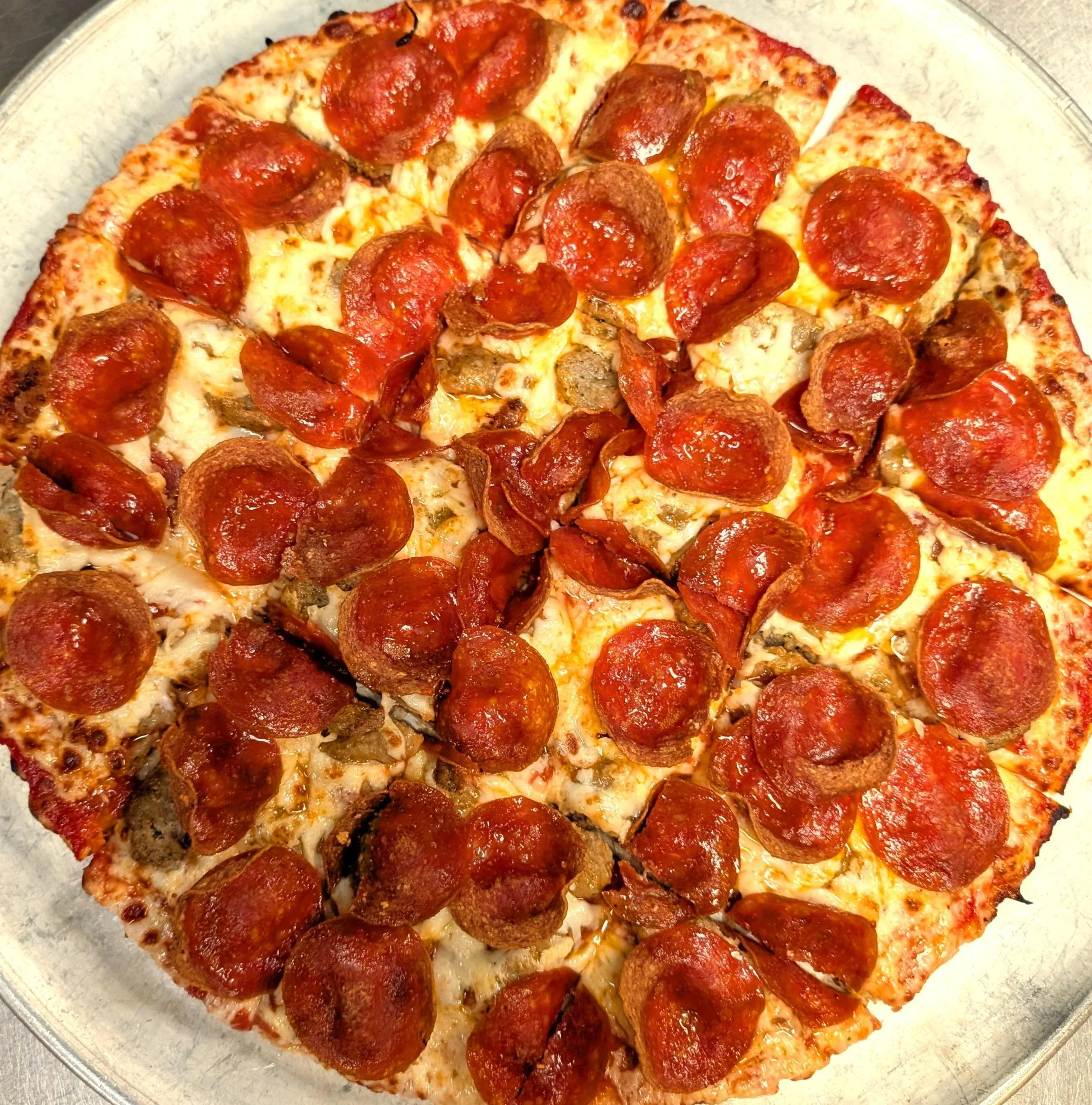 Pizza with pepperoni, sausage, and bacon on a glass plate.