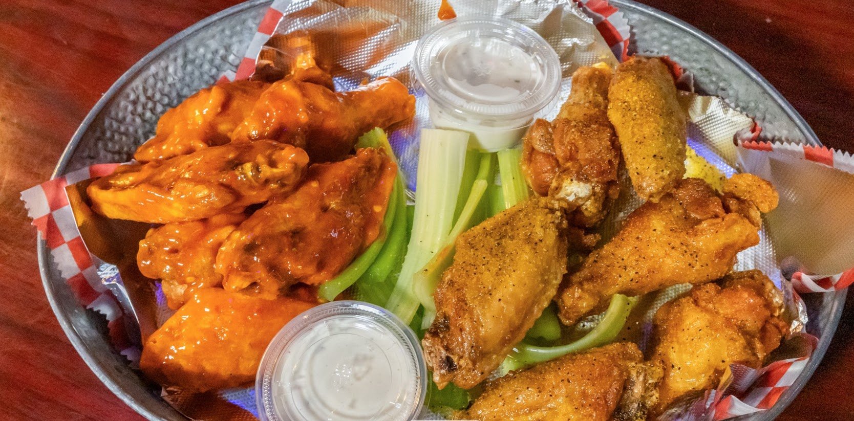 A metal tray with buffalo wings, fried chicken wings, celery sticks, and ranch dipping sauces.