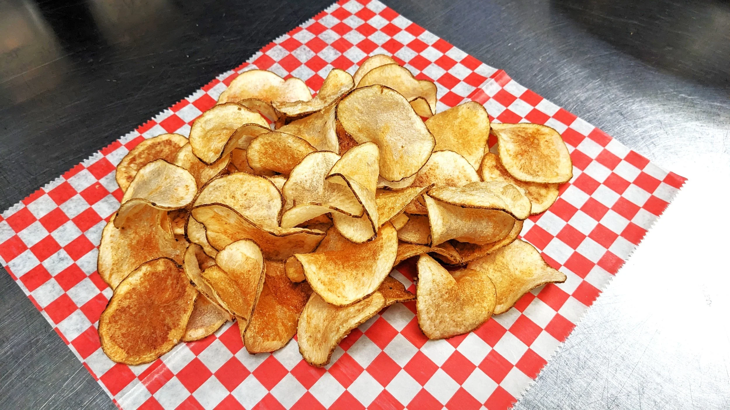 Crispy potato chips on red and white checkered paper.
