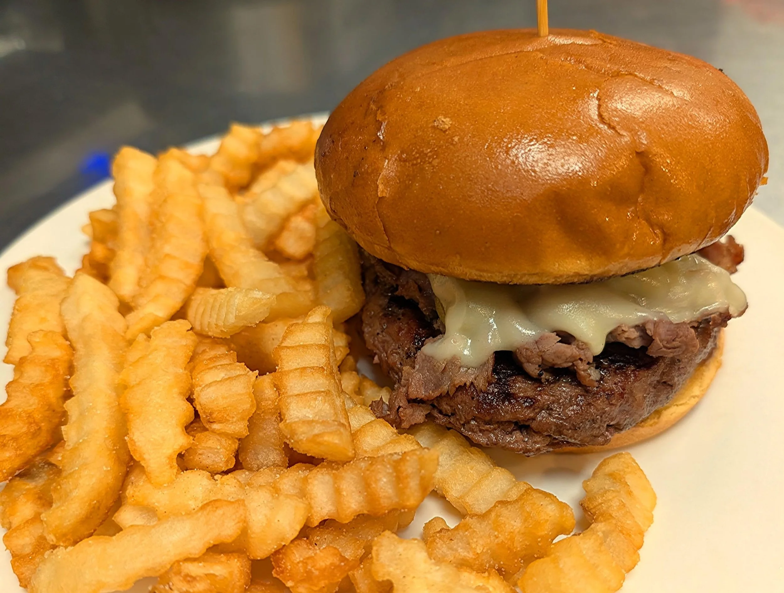 A plate with crinkle-cut French fries and a cheeseburger with a toasted bun, grilled beef patty, melted cheese, and bacon.