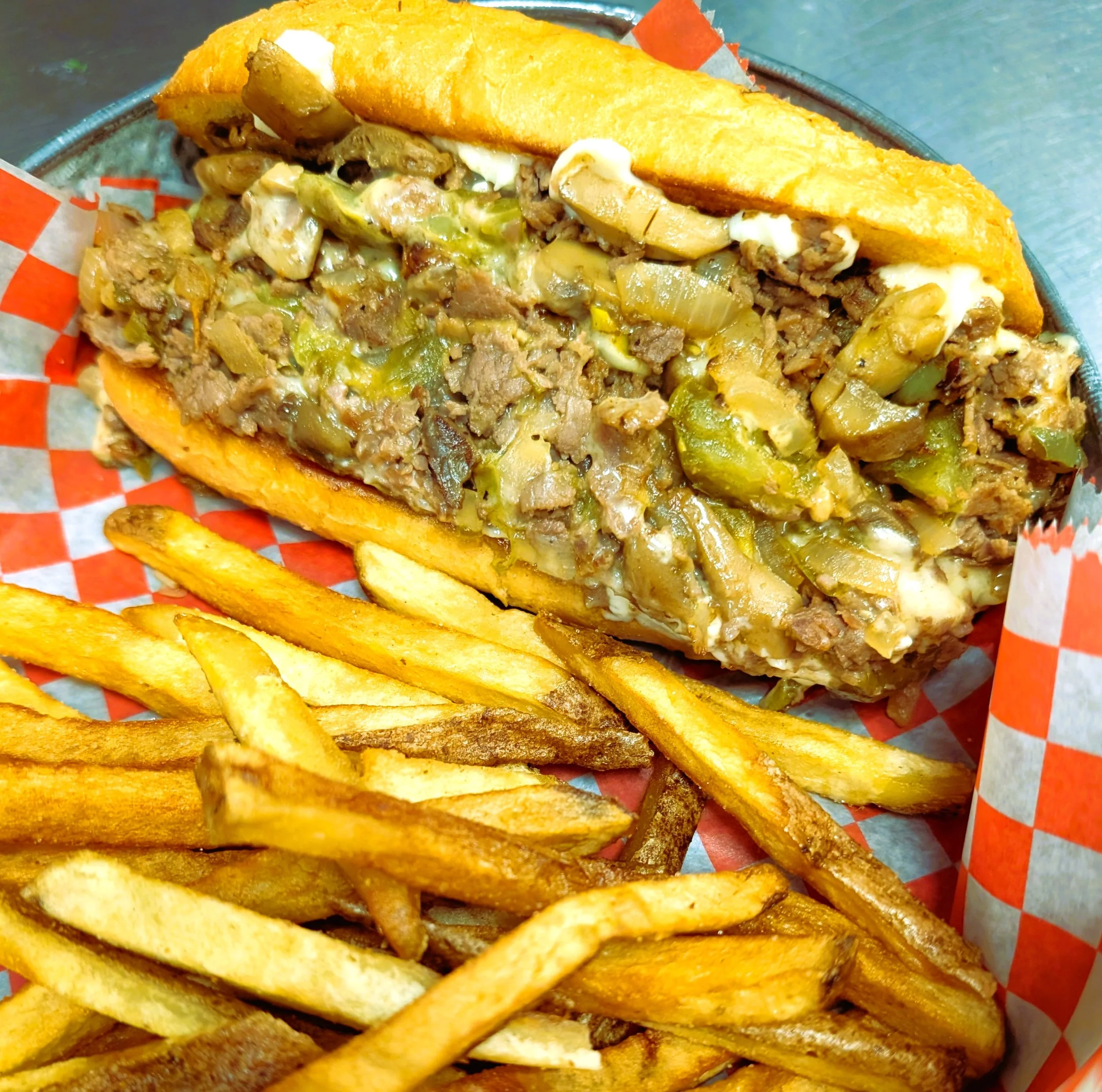Cheesesteak sandwich with onions and peppers served with French fries