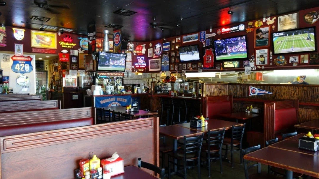 Interior of a sports bar with multiple televisions showing sports games, framed memorabilia and signs on the walls, and wooden tables and chairs for customers.
