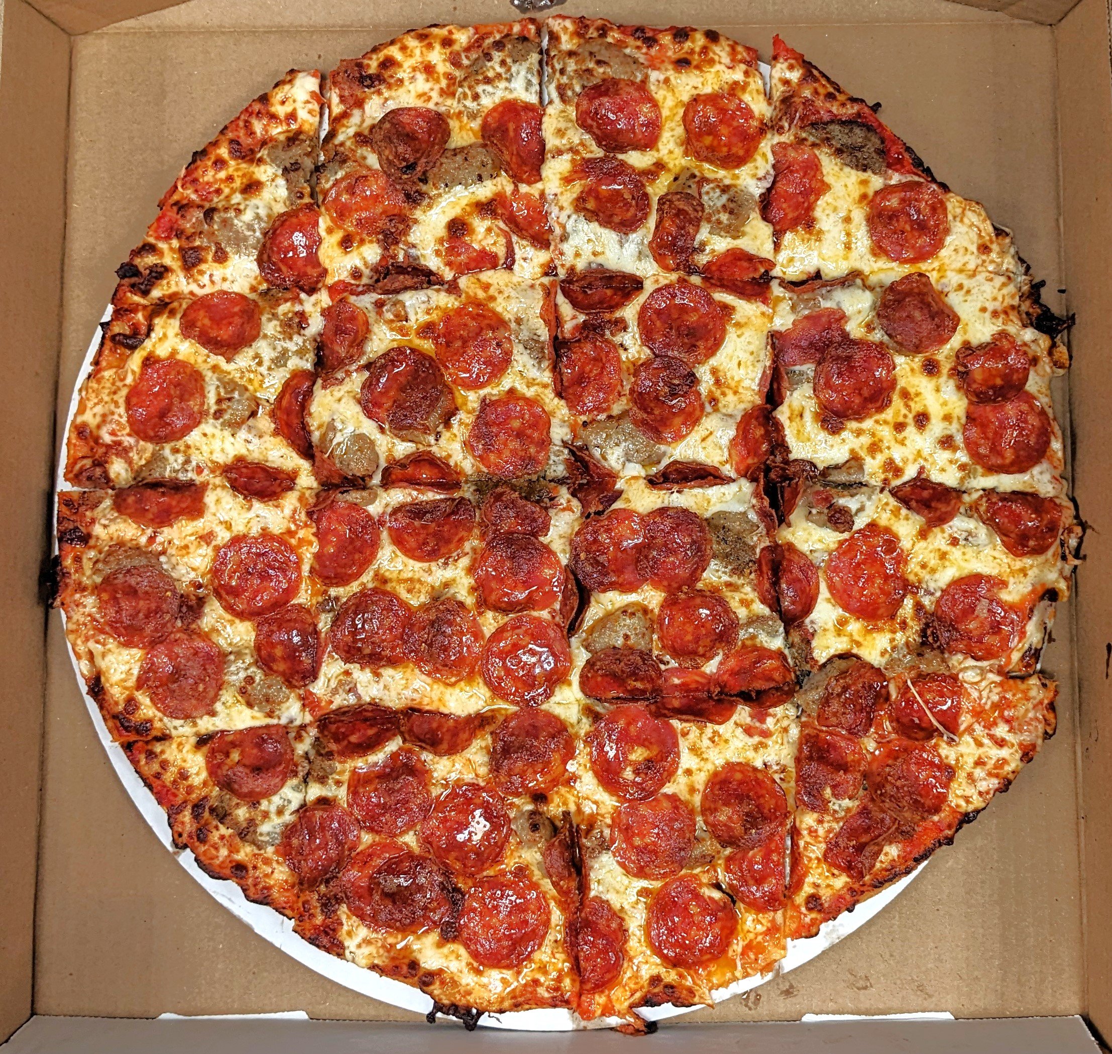 A pepperoni pizza in a cardboard box with cheese and sausage toppings.