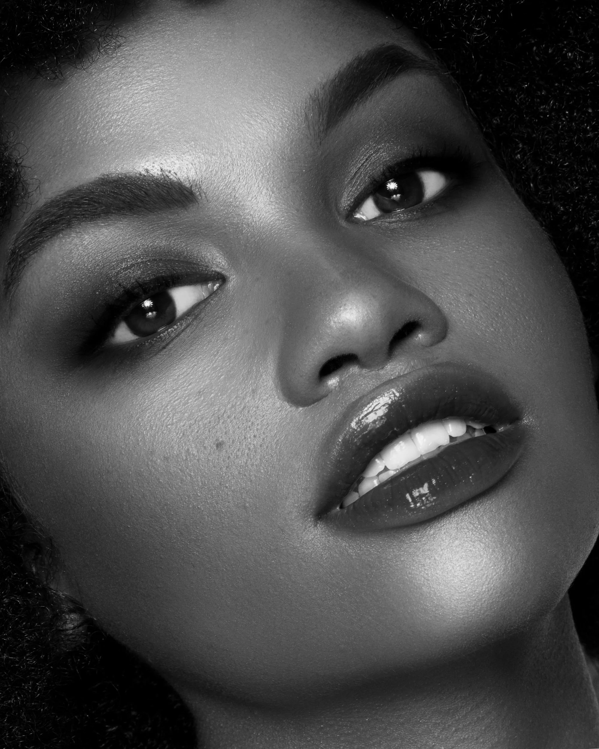 Close-up black and white photo of a woman's face showing only her eyes, nose, mouth, and eyebrow, with textured skin and facial features.