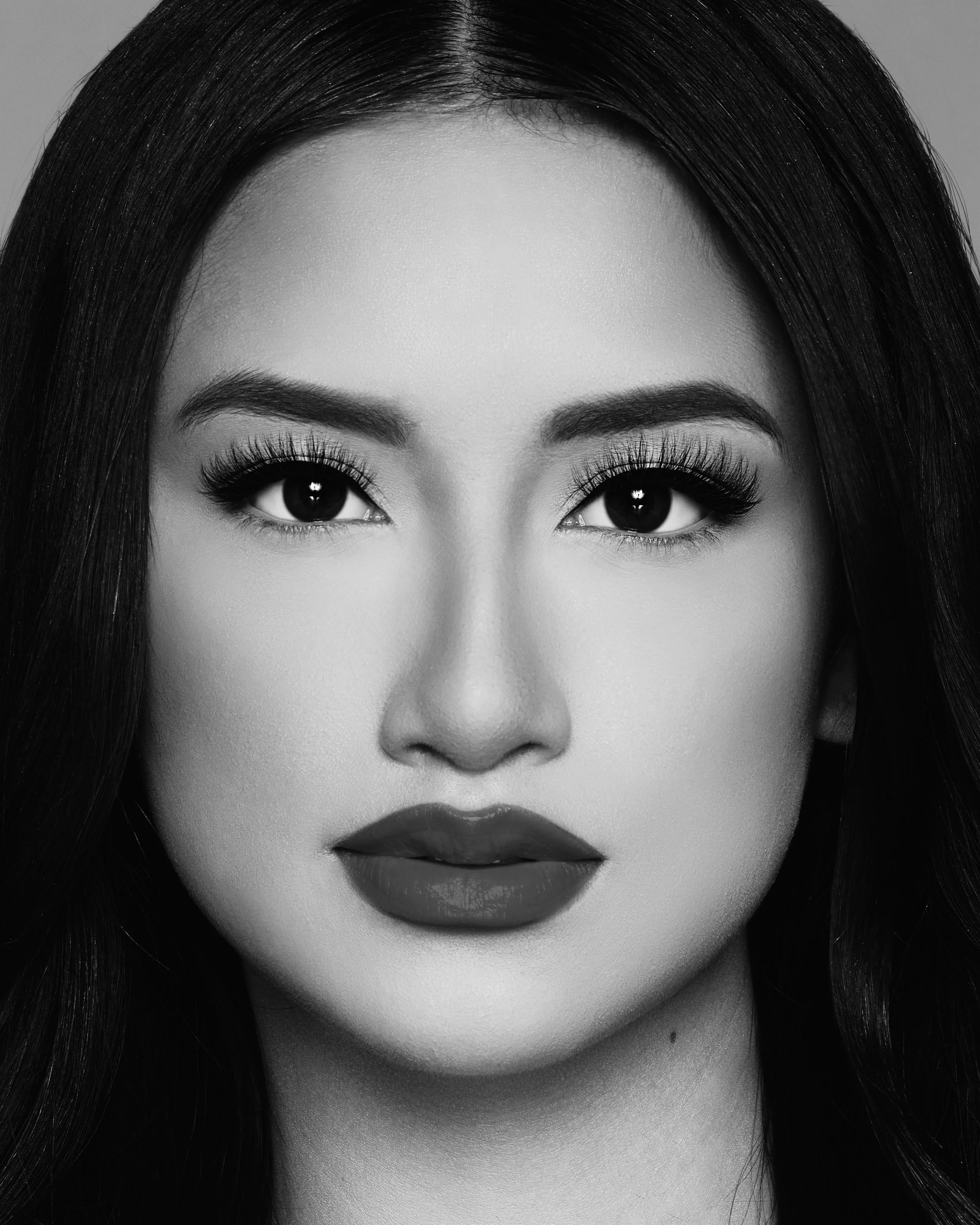 Close-up black-and-white portrait of a woman with dark hair, prominent eye makeup, and bold lipstick.