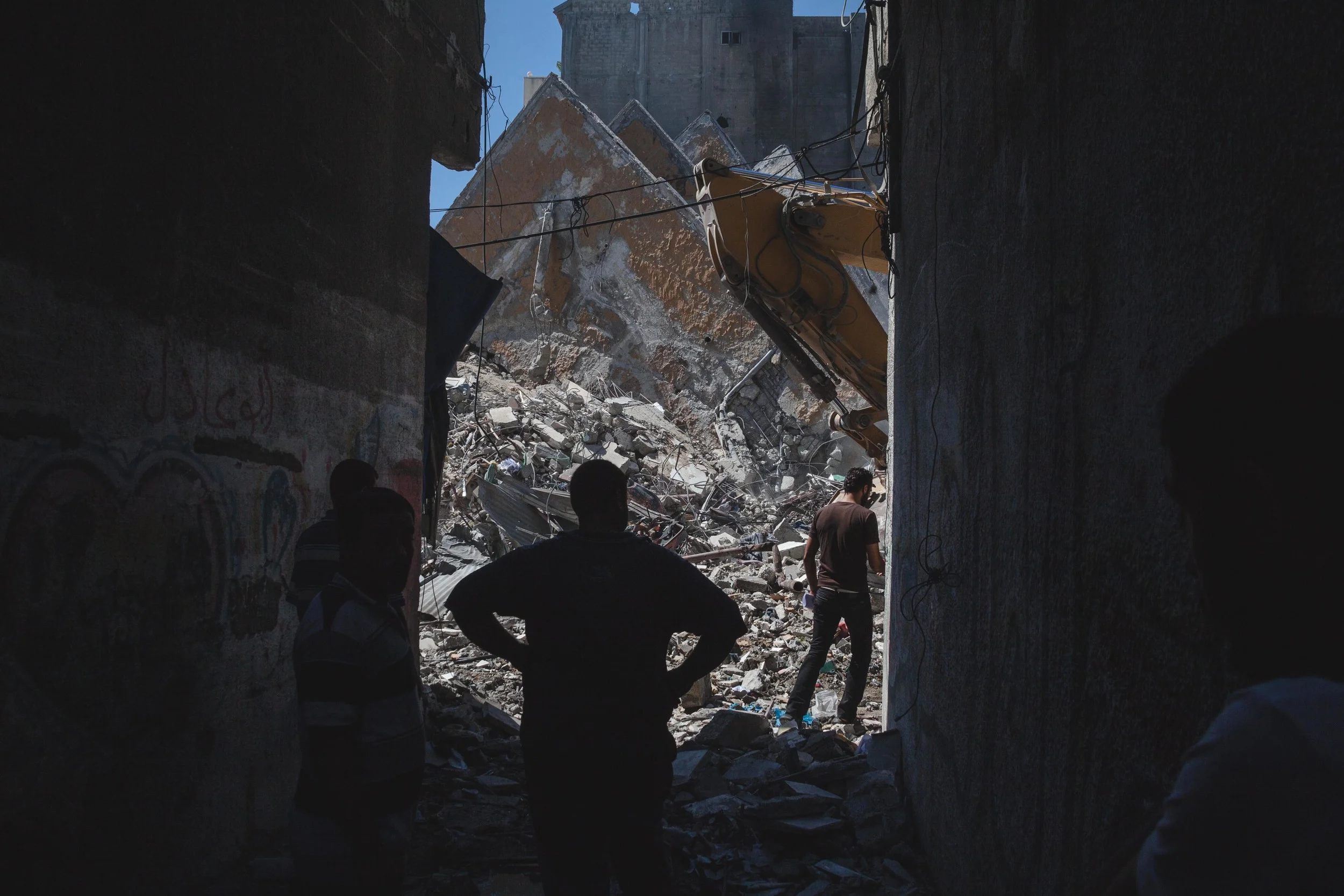 Bystanders watch as heavy machinery searches through the remains of Al-Basha tower in the center of Gaza City after it collapsed following an airstrike by Israel fighter planes. Residence of the 15 story residential building evacuated after receiving warnings of impending strike.