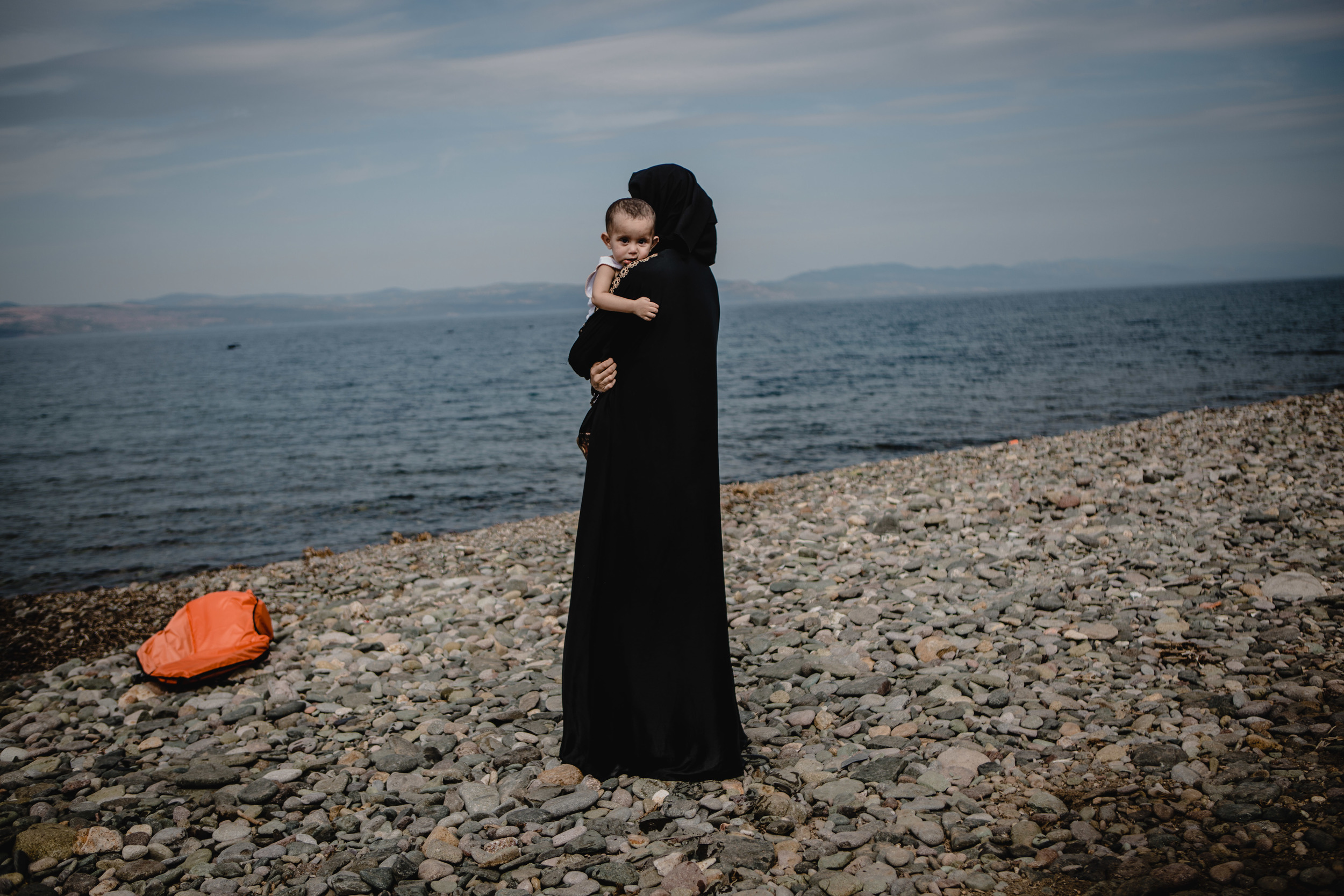  A women holds her child while looking back towards the sea she and her family just crossed from Turkey. 