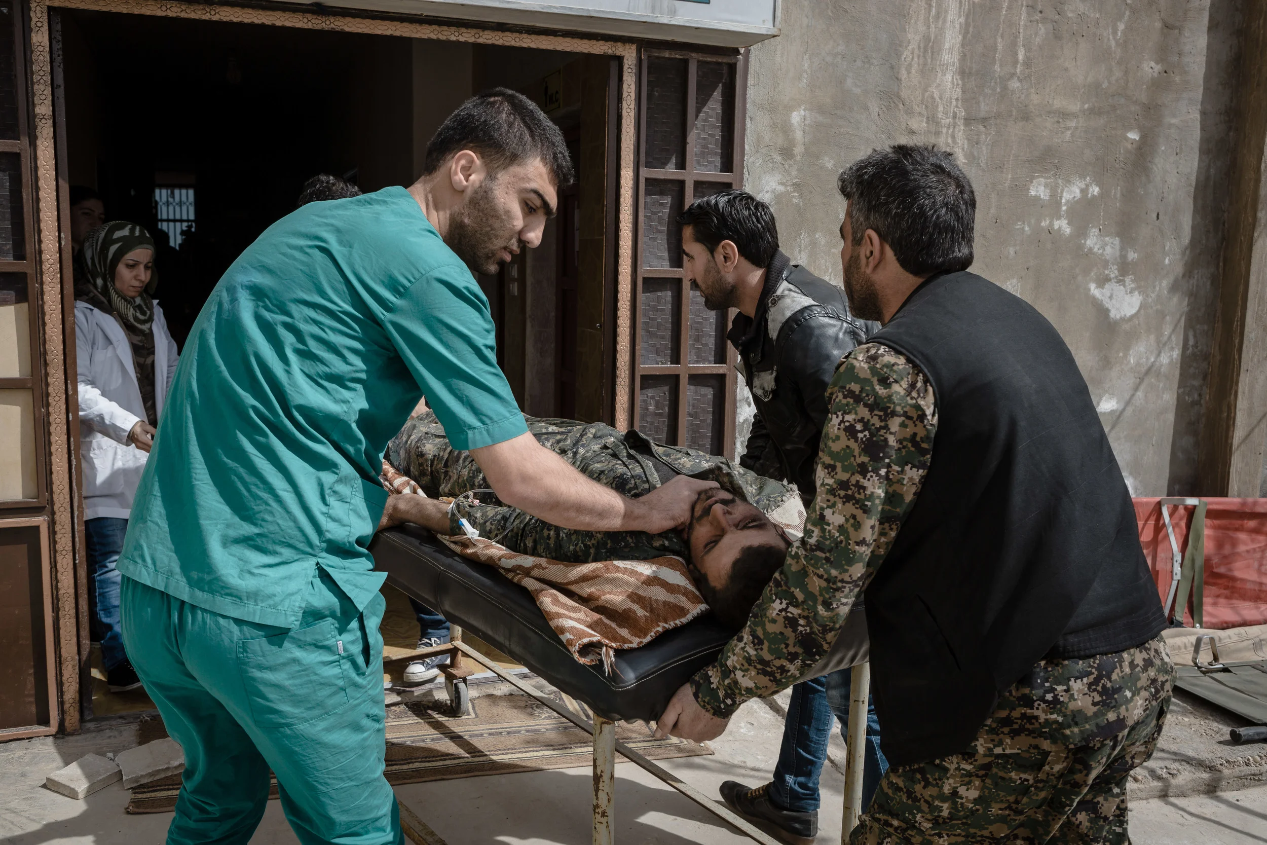 Doctors and fighters rush to bring the wounded fighters into the medical facility after an IED went off as the fighters were clearing a house in Shadadi.