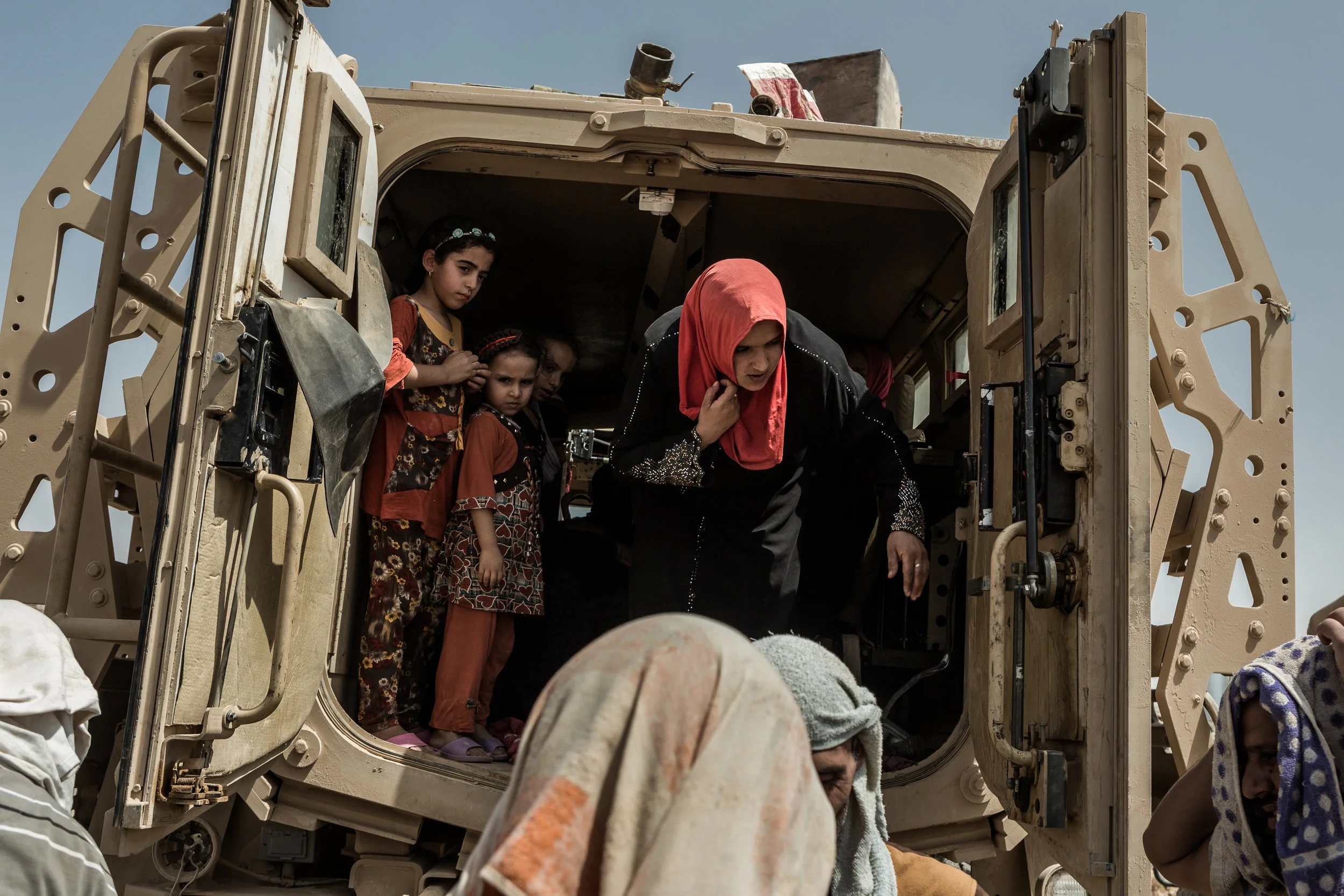 Displaced woman and children get out of a Iraqi armored vehicle once they arrive at a Peshmerga screening checkpoint near Makhmour, Iraq. When possible, the Iraqi army transports families to the screening point where they then wait for Kurdish forces to approve their transportation to UN camps set up inside Kurdish-controlled territory.