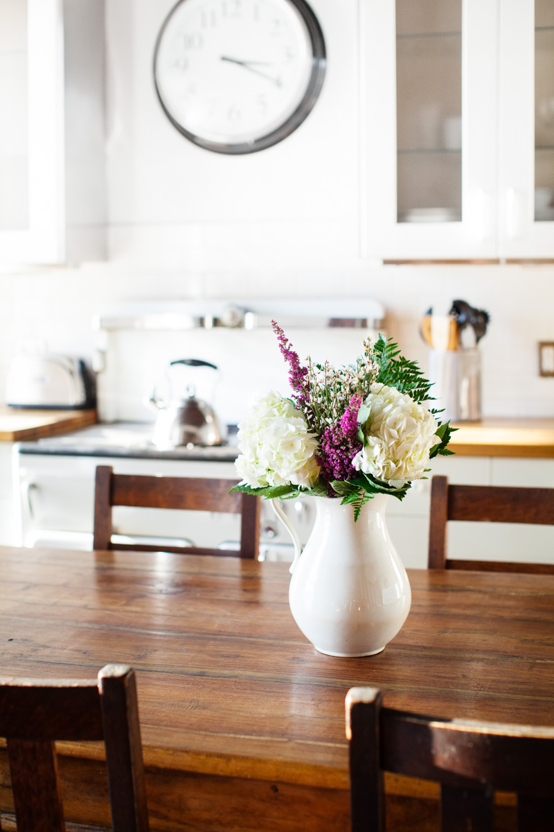 Fresh cut flowers sit in a white pitcher on the dining table.