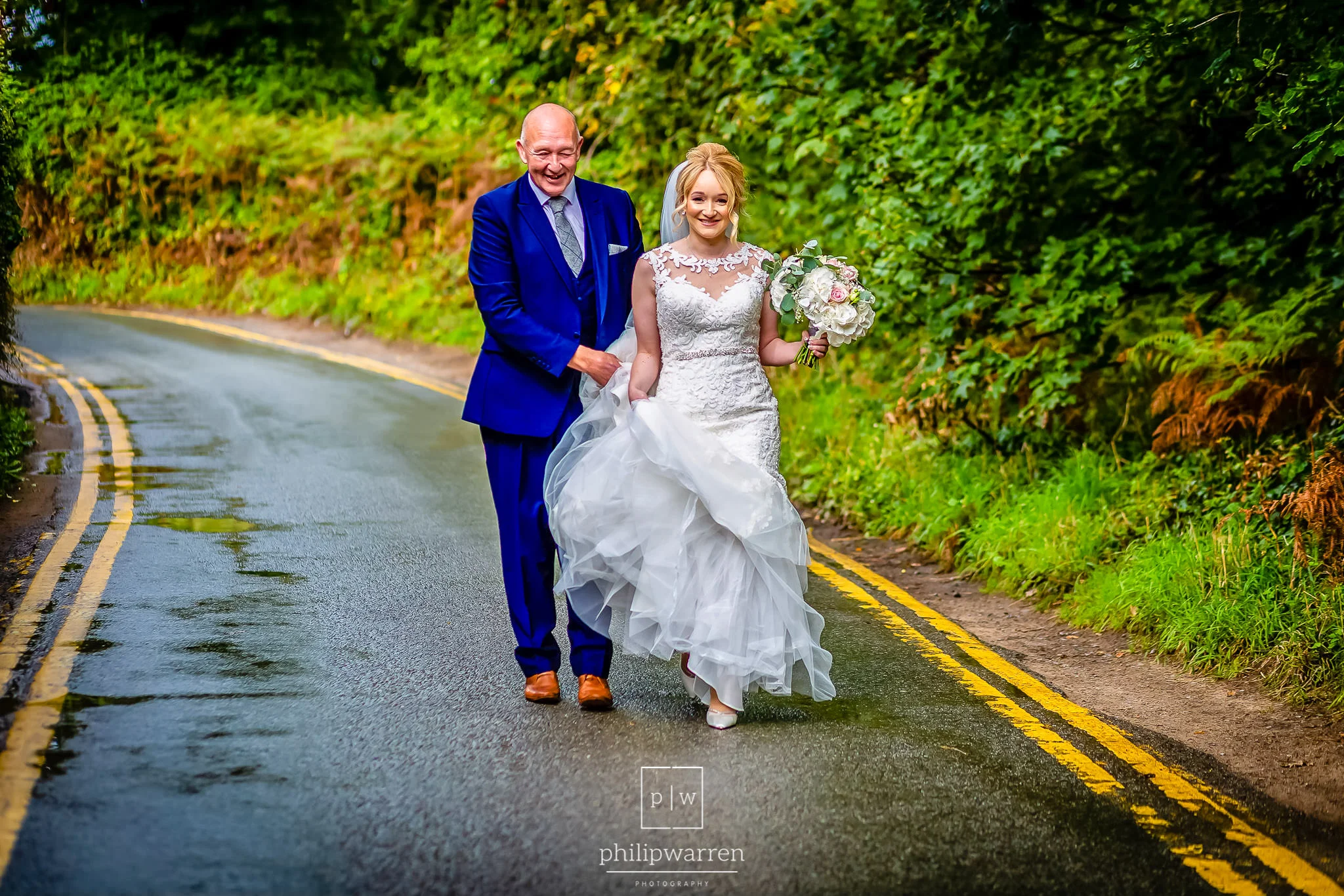 father of the bride carrying her wedding dress walking to the ce